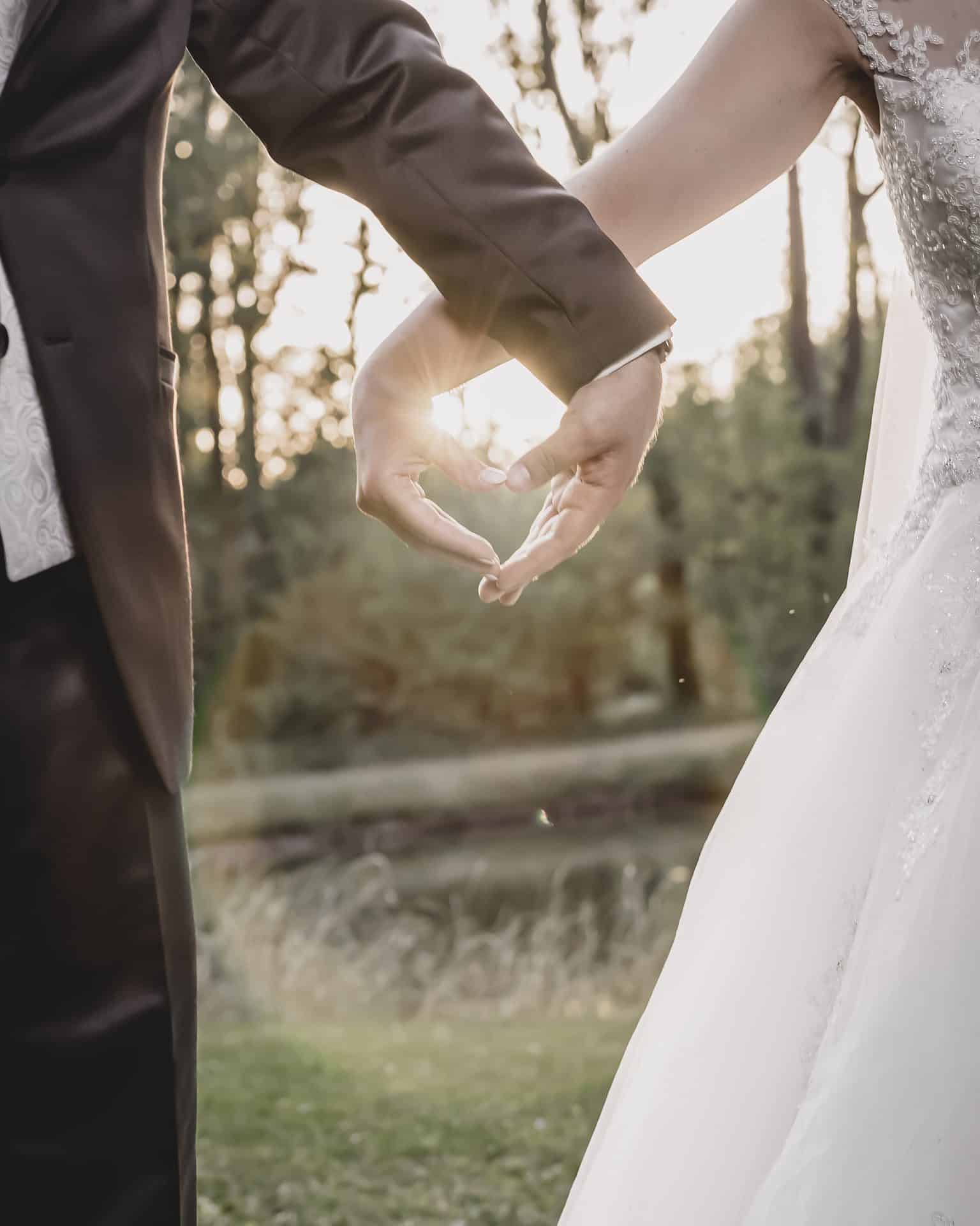 Eine Braut und ein Bräutigam formen mit ihren Händen ein Herz.