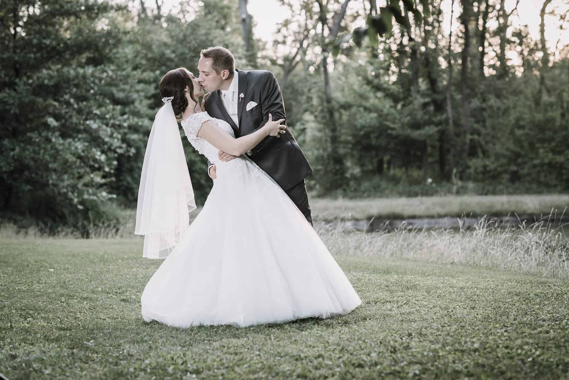 Eine Braut und ein Bräutigam küssen sich vor einem Teich.