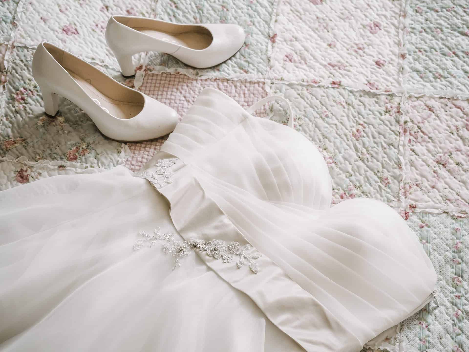 Ein weißes Hochzeitskleid und weiße Schuhe auf einer Steppdecke.