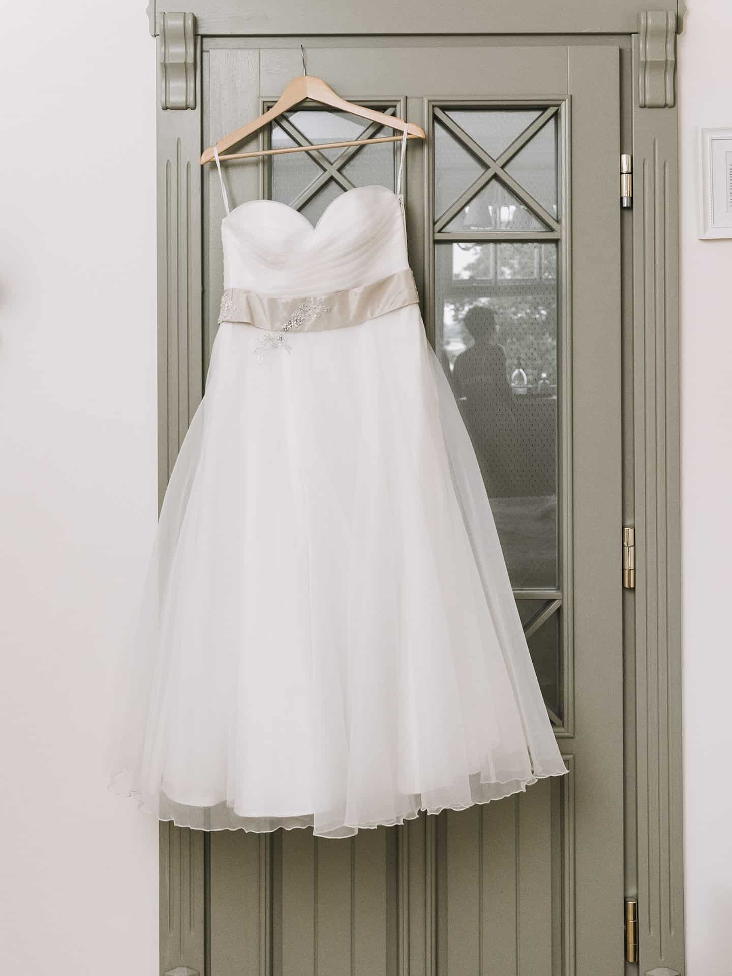 Ein weißes Hochzeitskleid hängt an einer Tür.