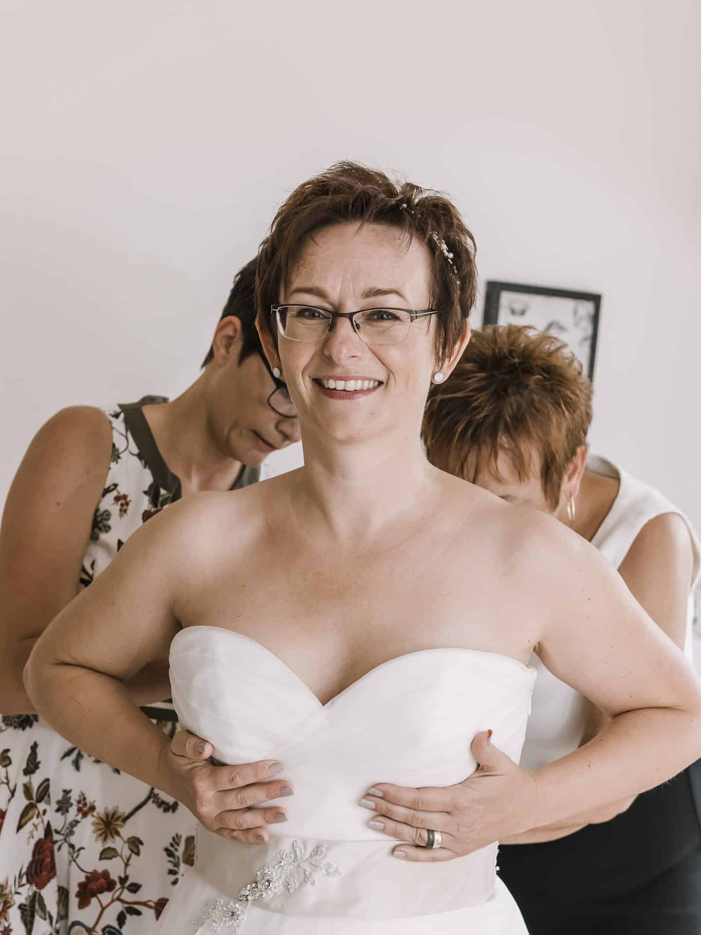 Eine Frau hilft einer anderen Frau, ihr Hochzeitskleid anzuziehen.