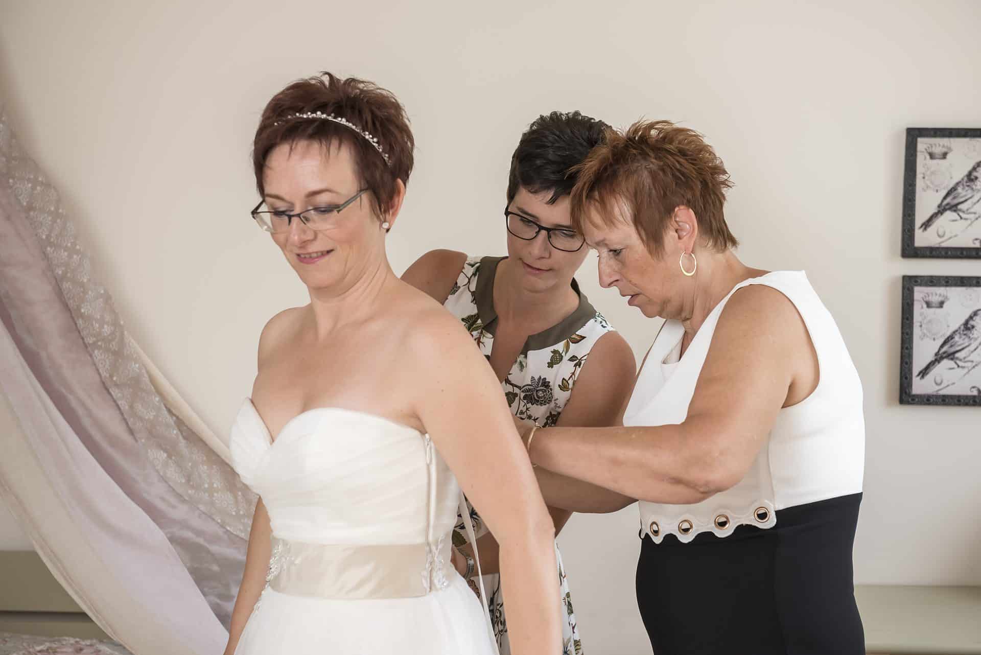 Eine Frau hilft einer anderen Frau beim Anziehen eines Hochzeitskleides.