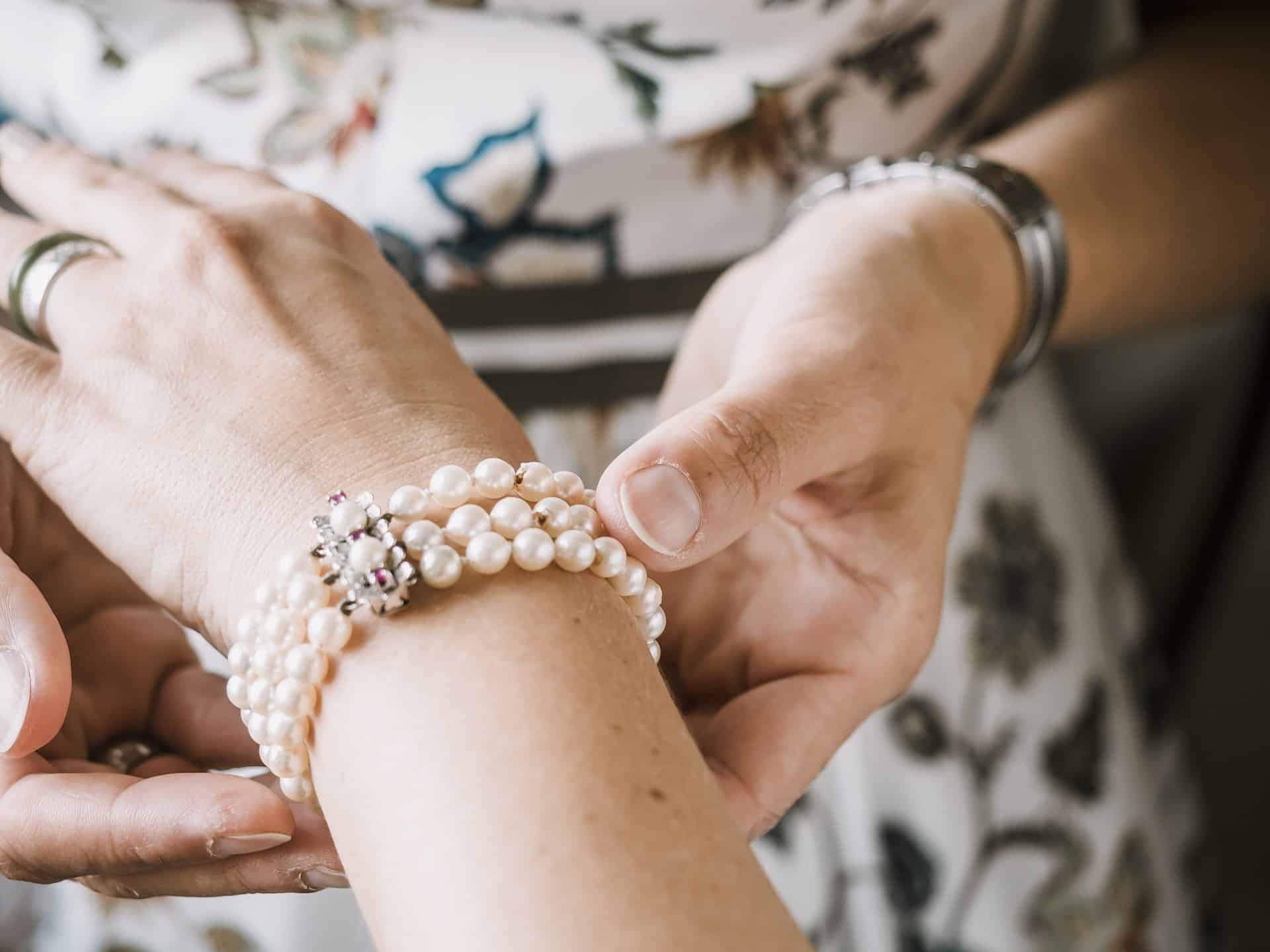 Eine Frau legt einer Frau ein Perlenarmband um das Handgelenk.