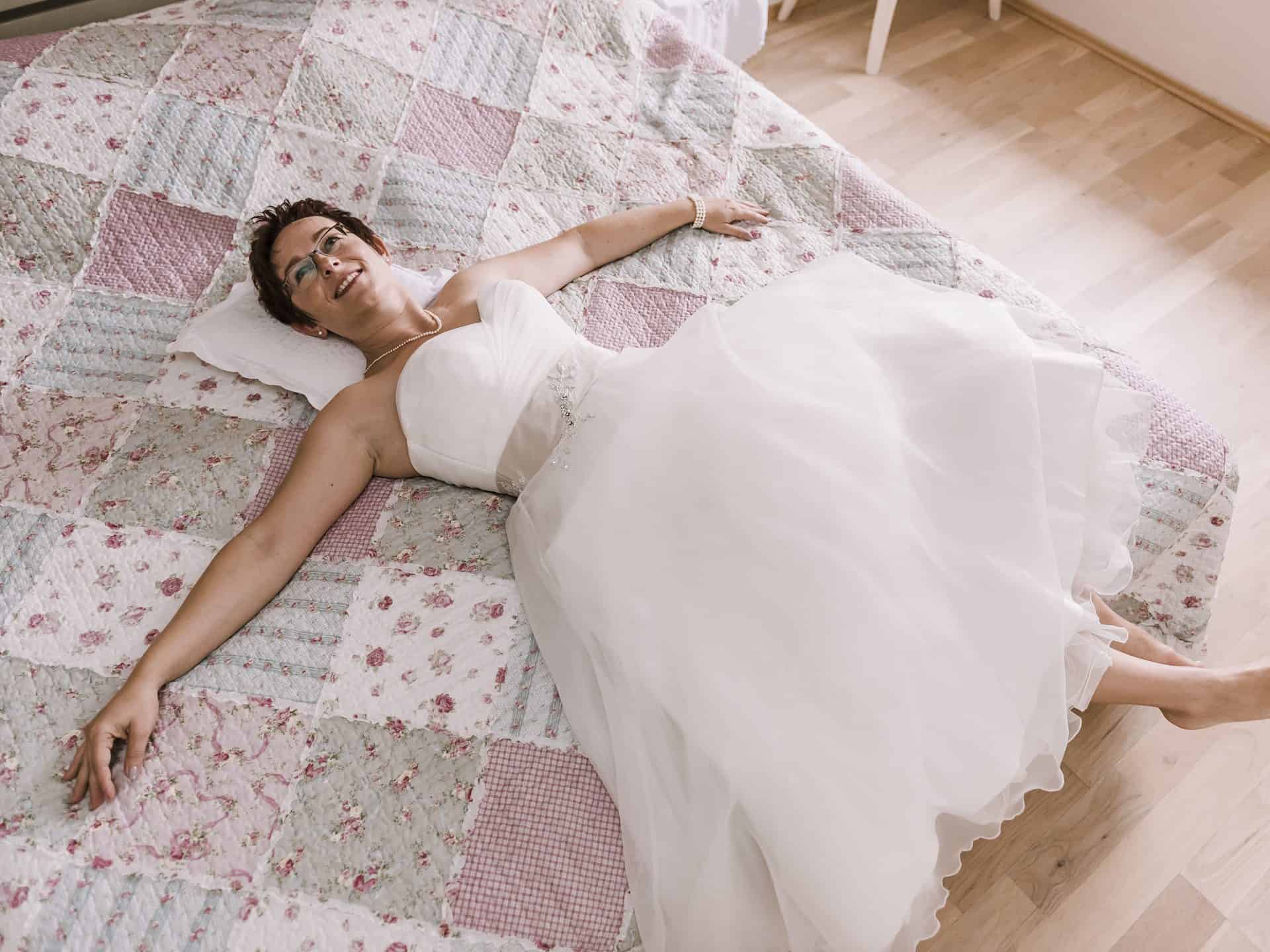 Eine Frau in einem Hochzeitskleid liegt auf einem Bett.