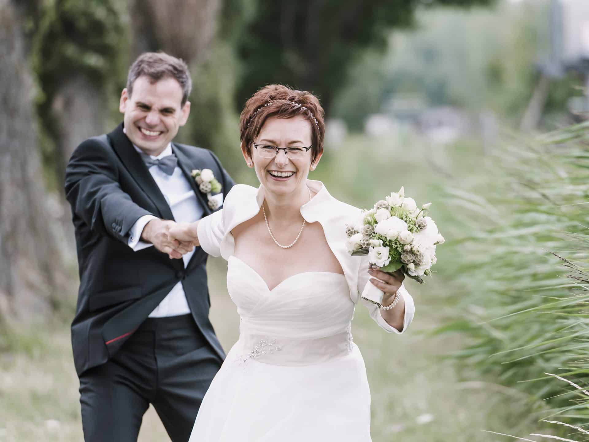Eine Braut und ein Bräutigam laufen durch ein Feld.