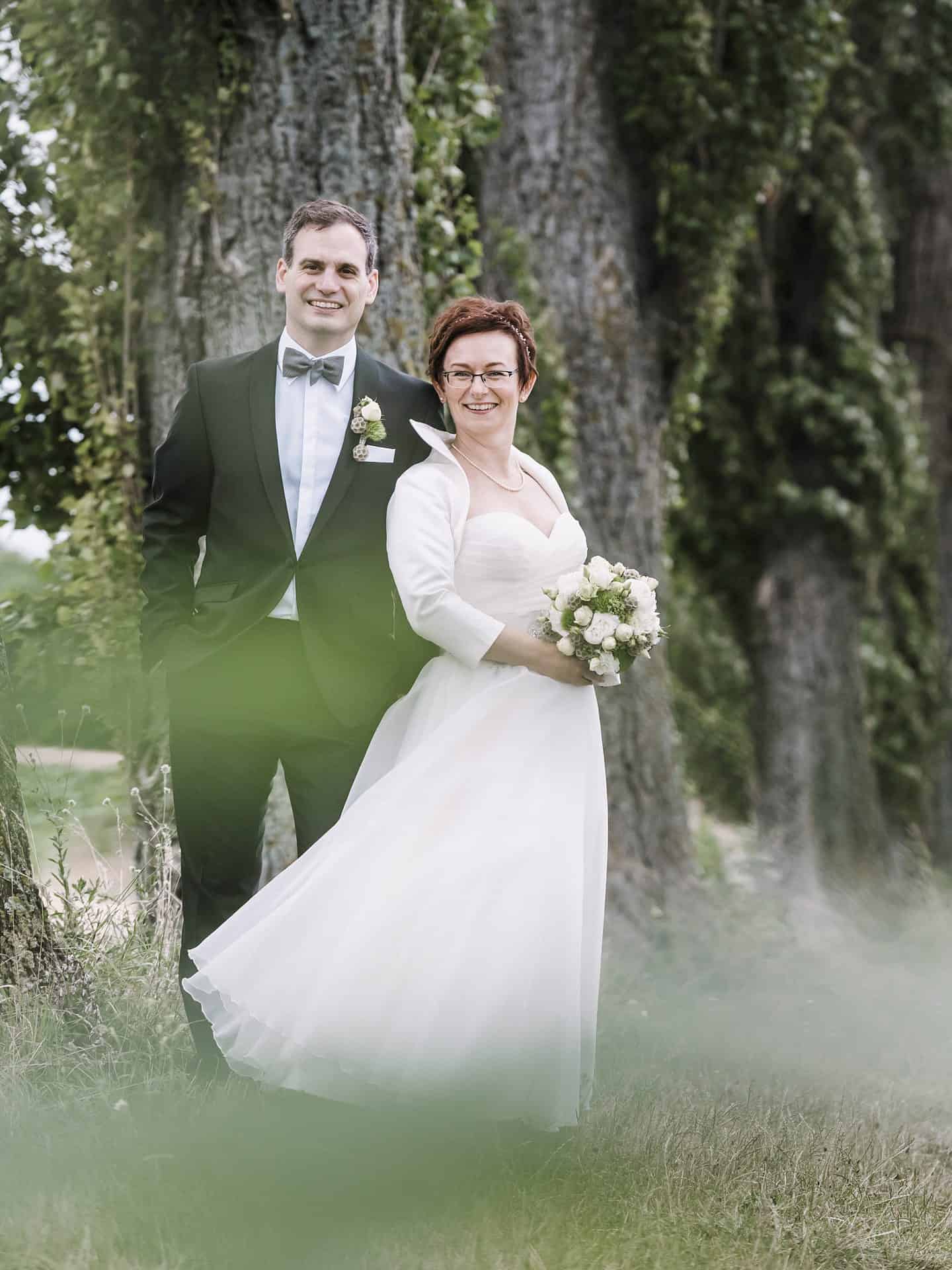 Eine Braut und ein Bräutigam posieren vor Bäumen.