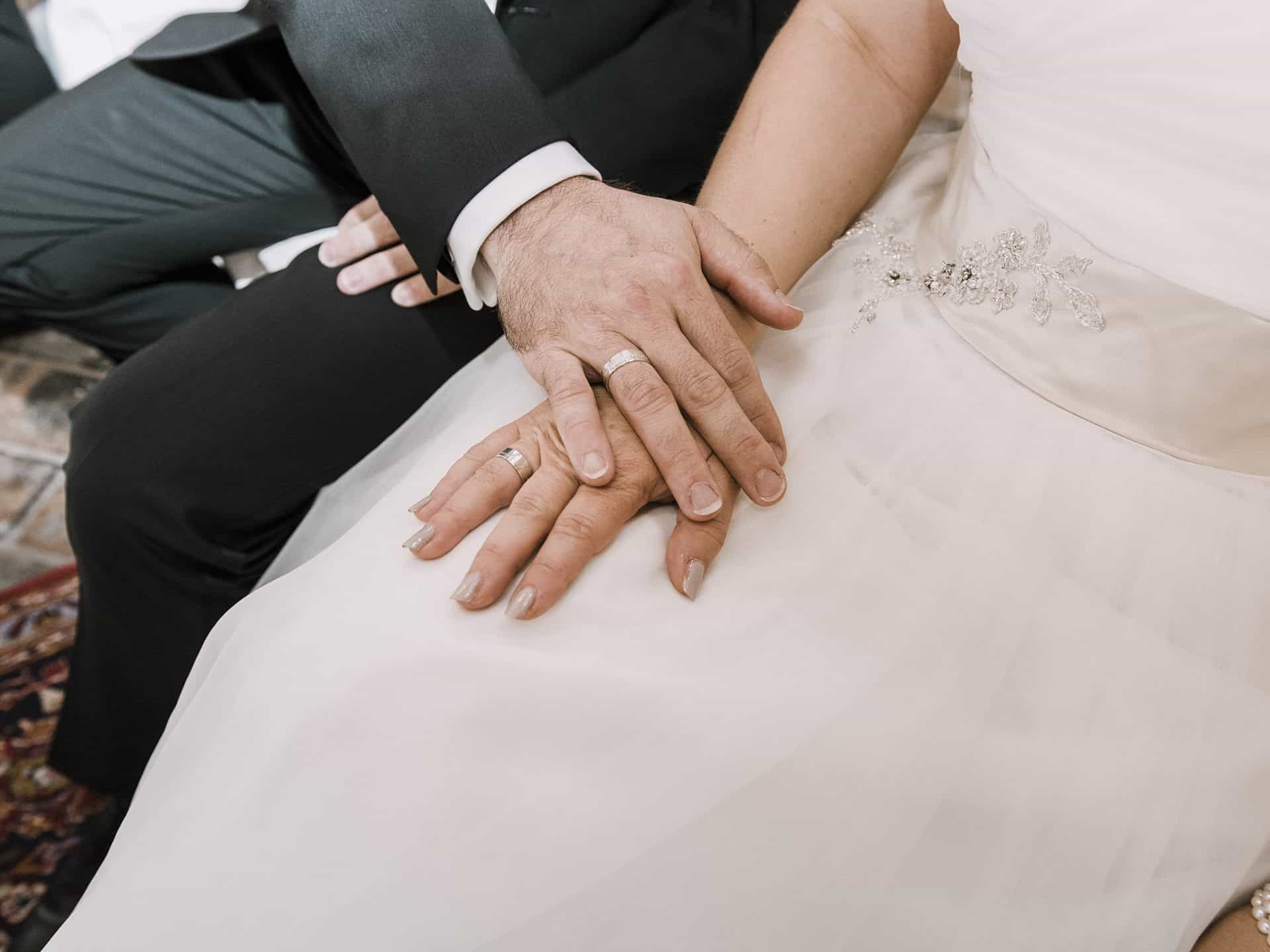 Die Hände eines Brautpaares sitzen auf einem Teppich.