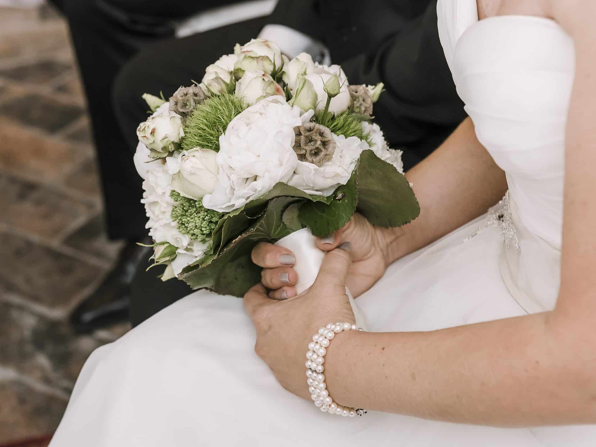 Eine Braut hält einen Strauß weißer und grüner Blumen.