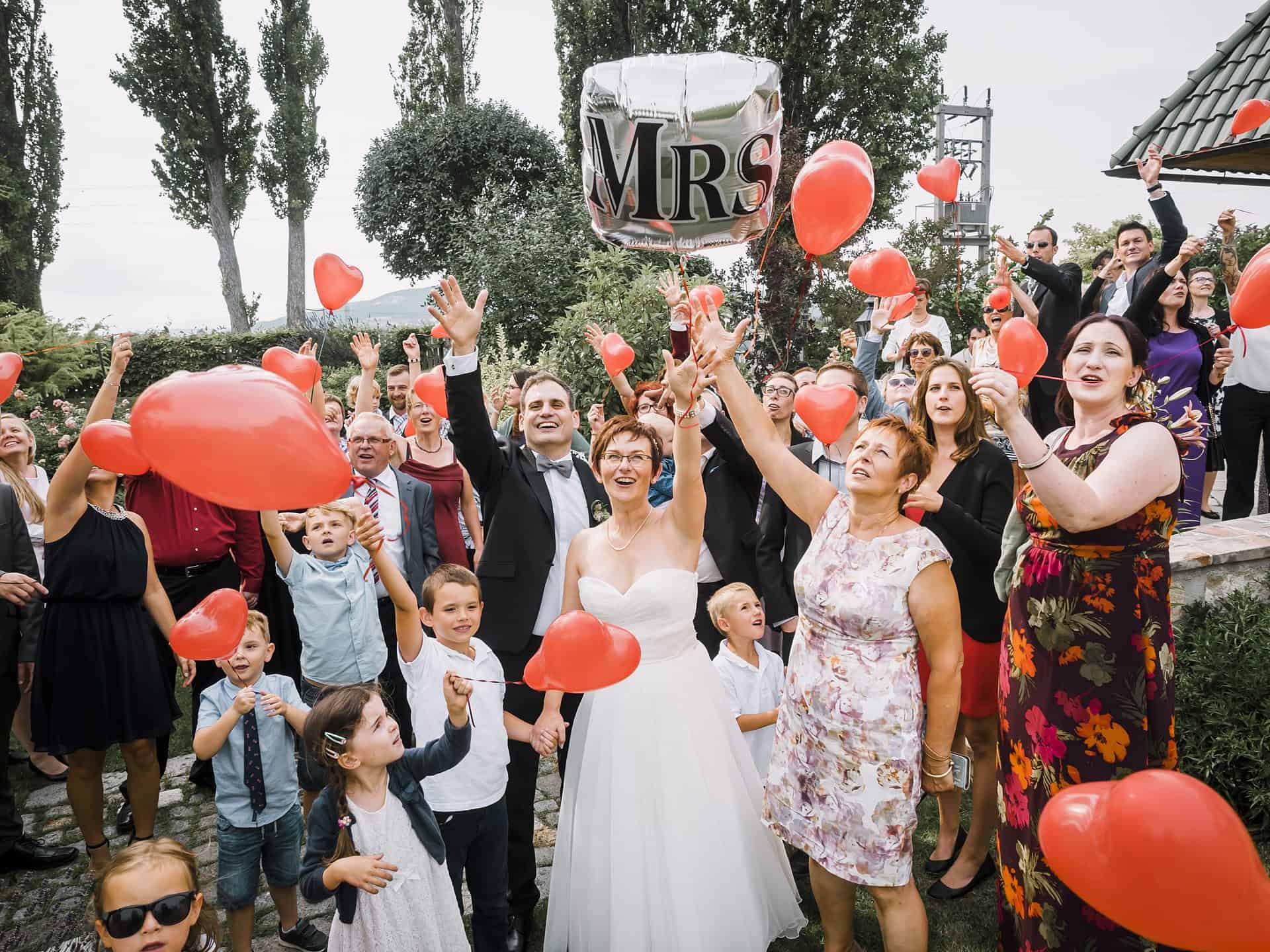 Eine Gruppe von Menschen hält bei einer Hochzeit rote Luftballons in der Hand.