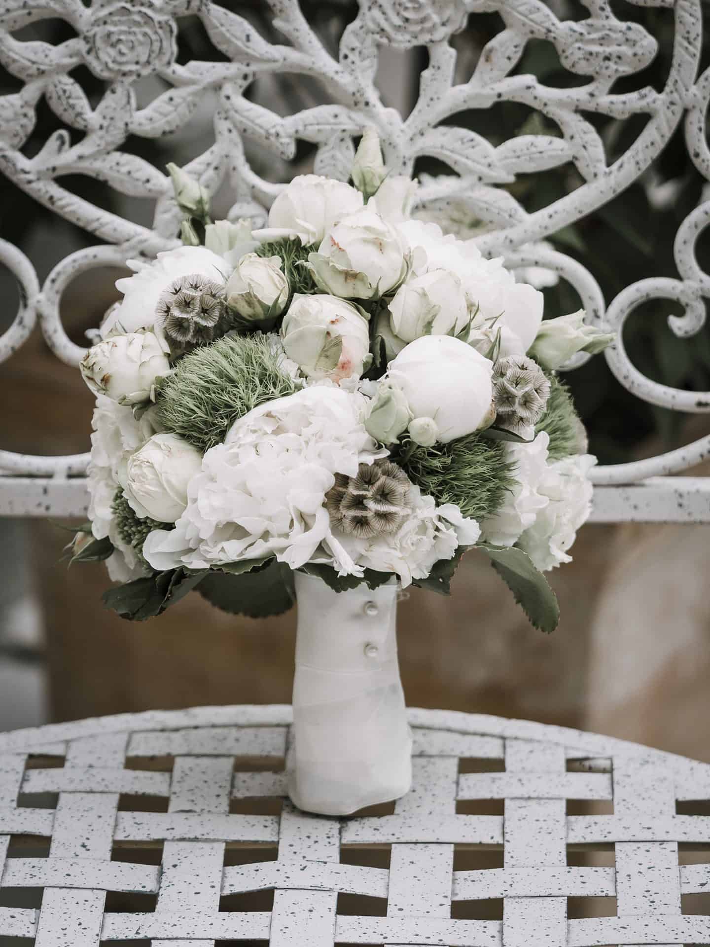Auf einem Metallstuhl sitzt ein weiß-grüner Blumenstrauß.