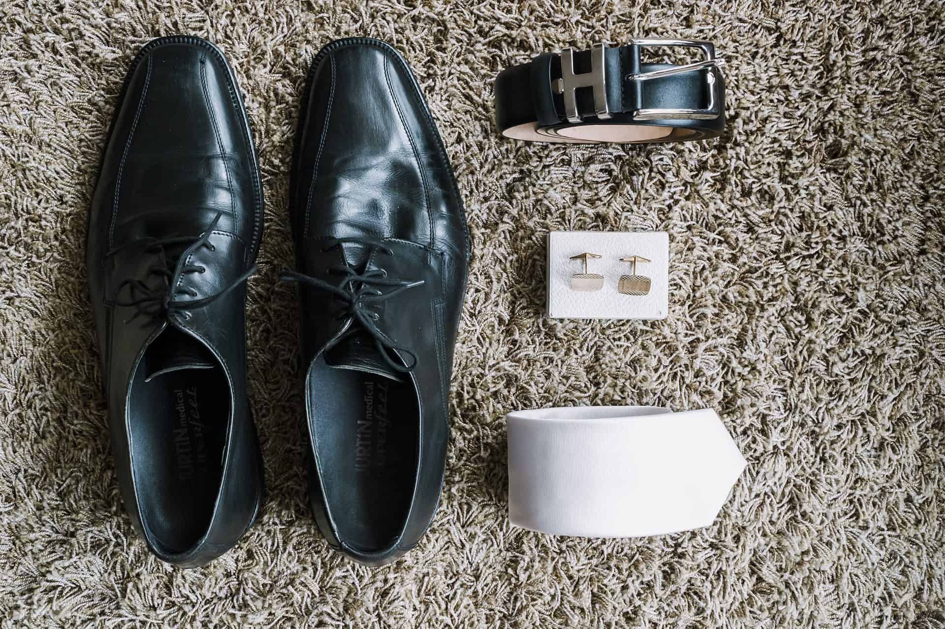 Ein Paar schwarze Schuhe, eine Uhr und Manschettenknöpfe auf einem Teppich.