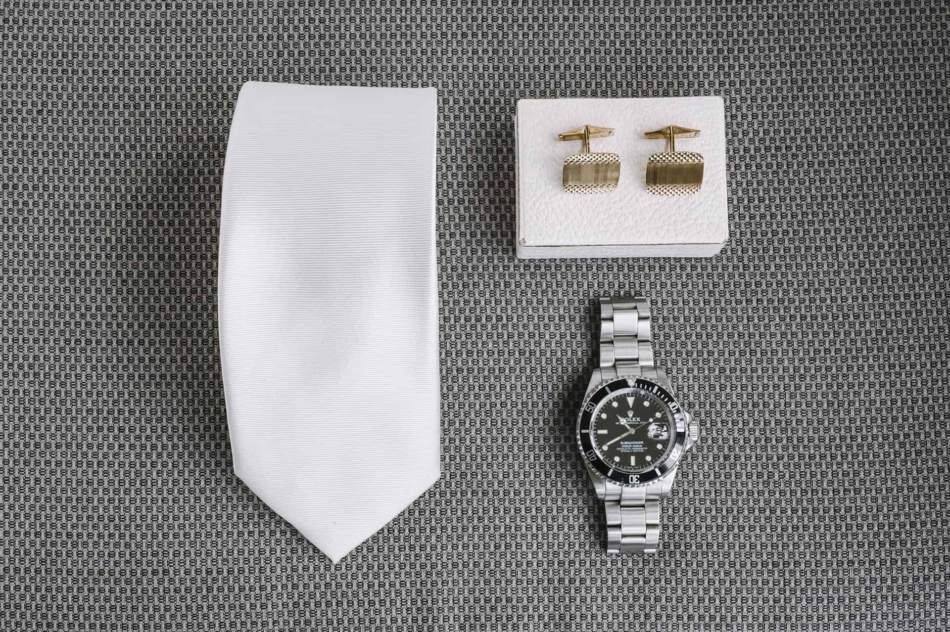 Auf einem Tisch liegen eine Uhr, eine Krawatte und Manschettenknöpfe.