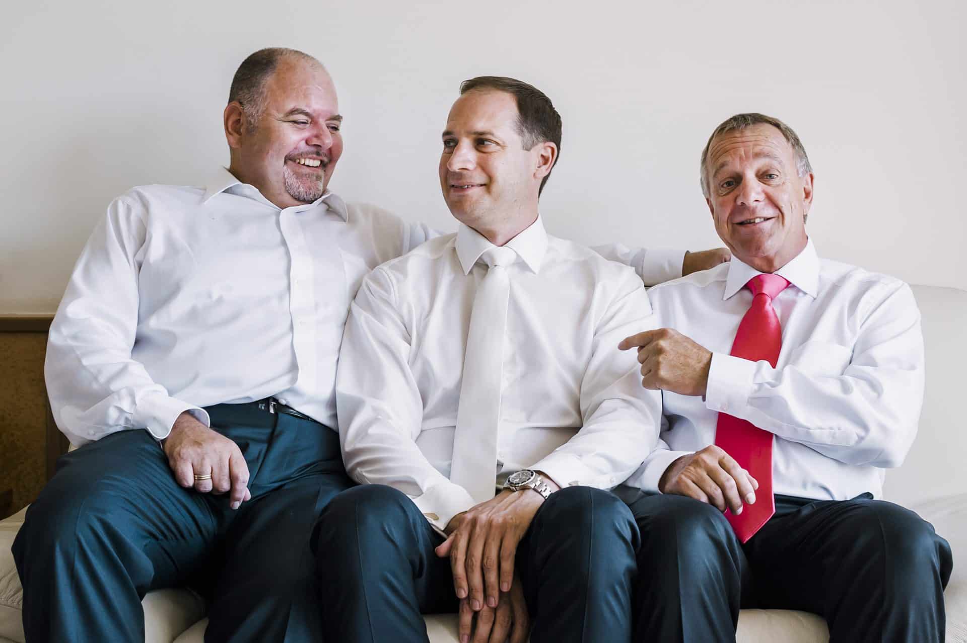 Drei Männer mit Krawatte sitzen auf einer Couch.