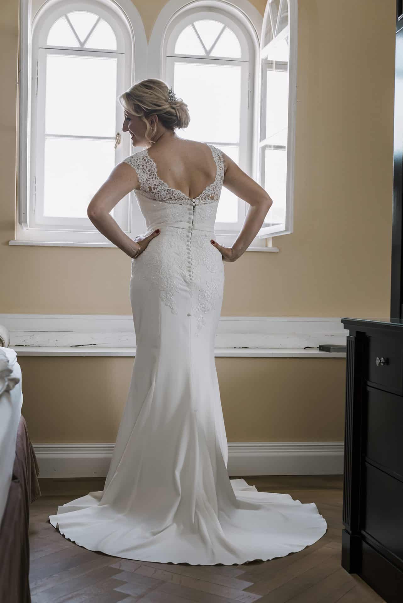 Eine Frau in einem Hochzeitskleid steht vor einem Fenster.