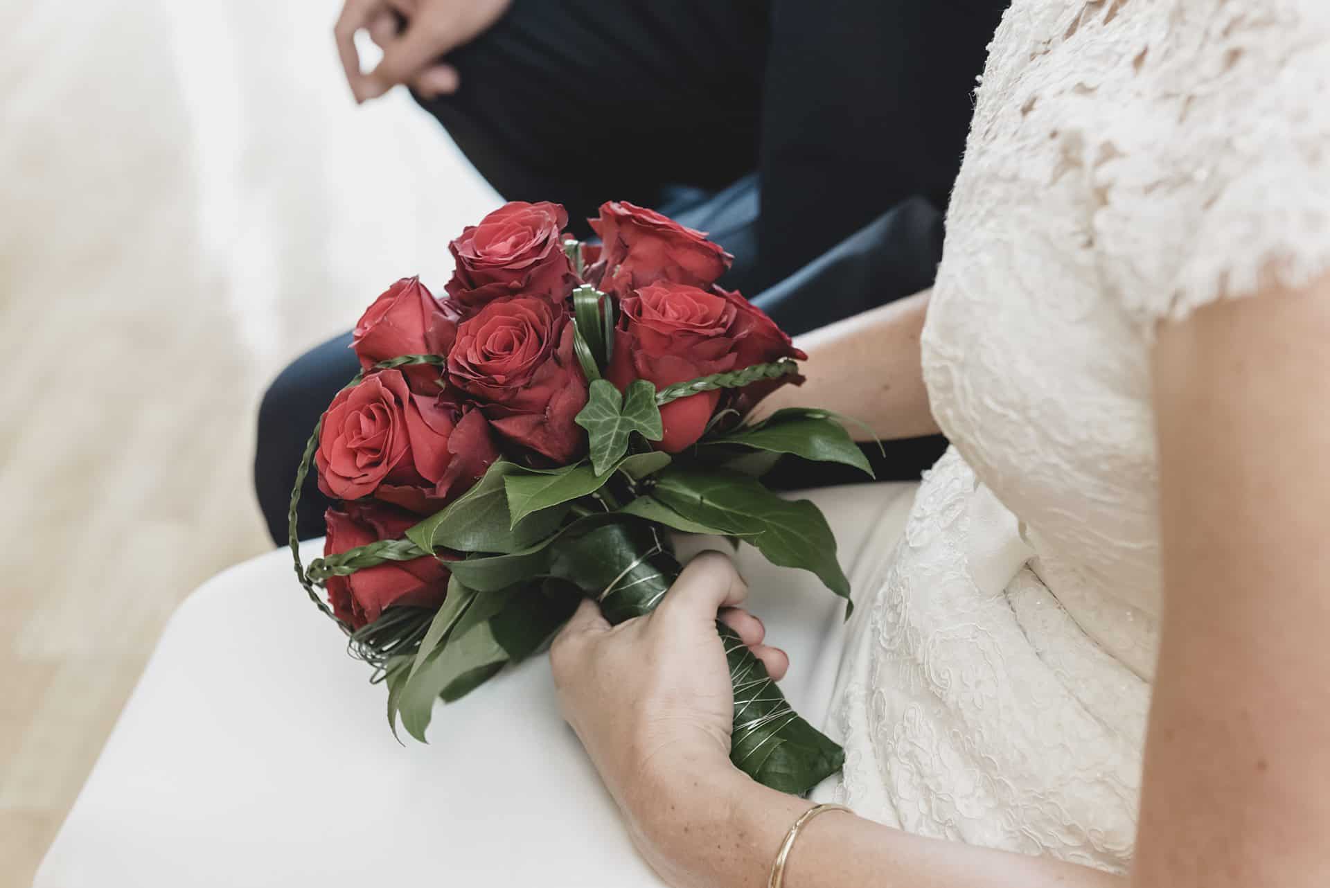 Eine Braut hält einen Strauß roter Rosen.