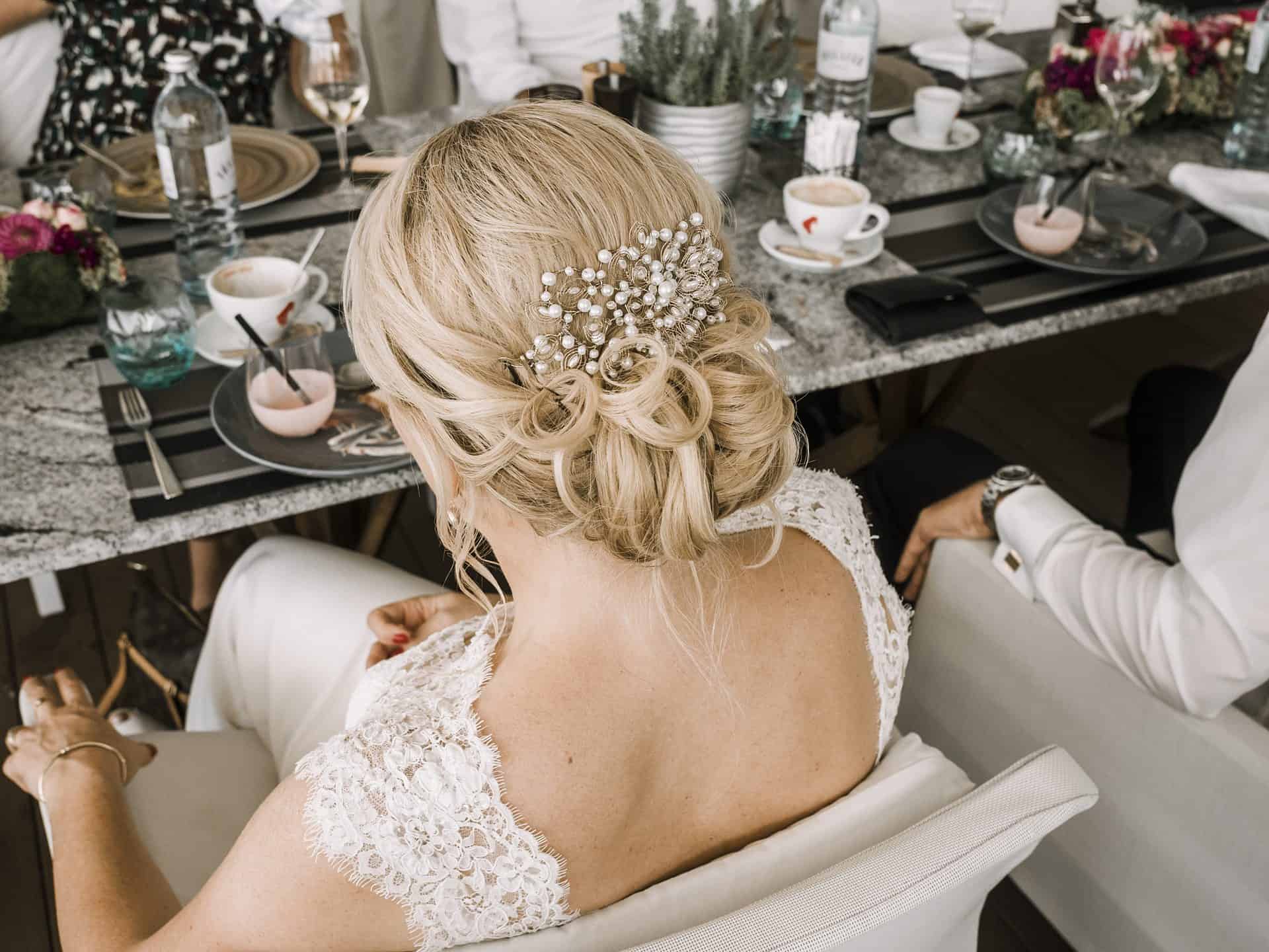 Eine Braut sitzt mit einem Haarkamm auf dem Kopf an einem Tisch.