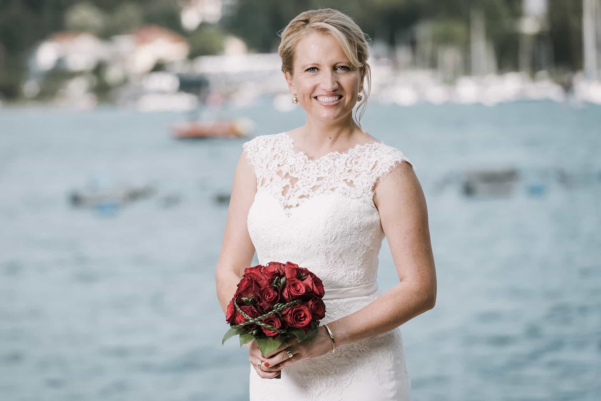 Eine Braut hält einen Blumenstrauß vor einem See.
