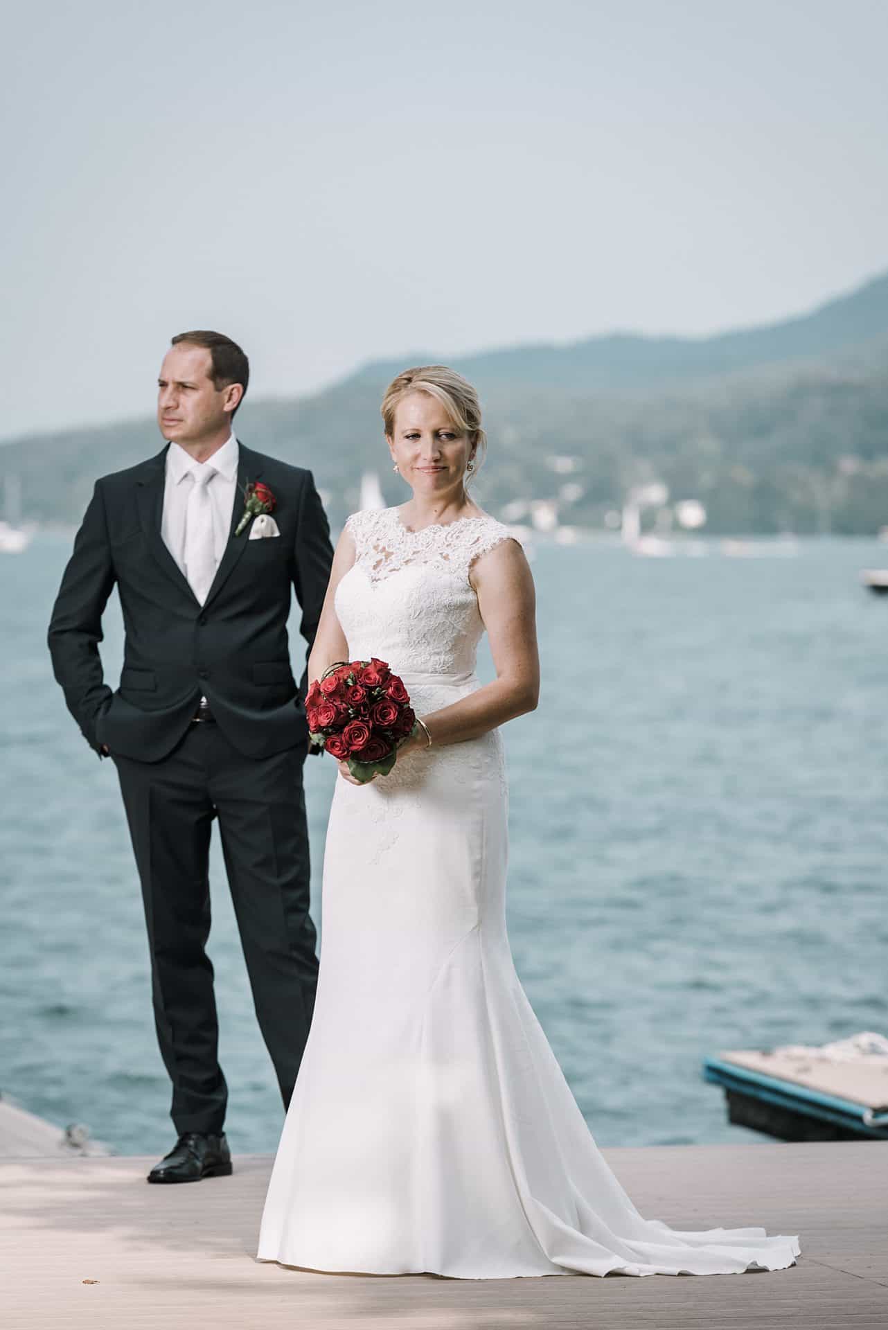 Eine Braut und ein Bräutigam stehen auf einem Steg, im Hintergrund ein Boot.