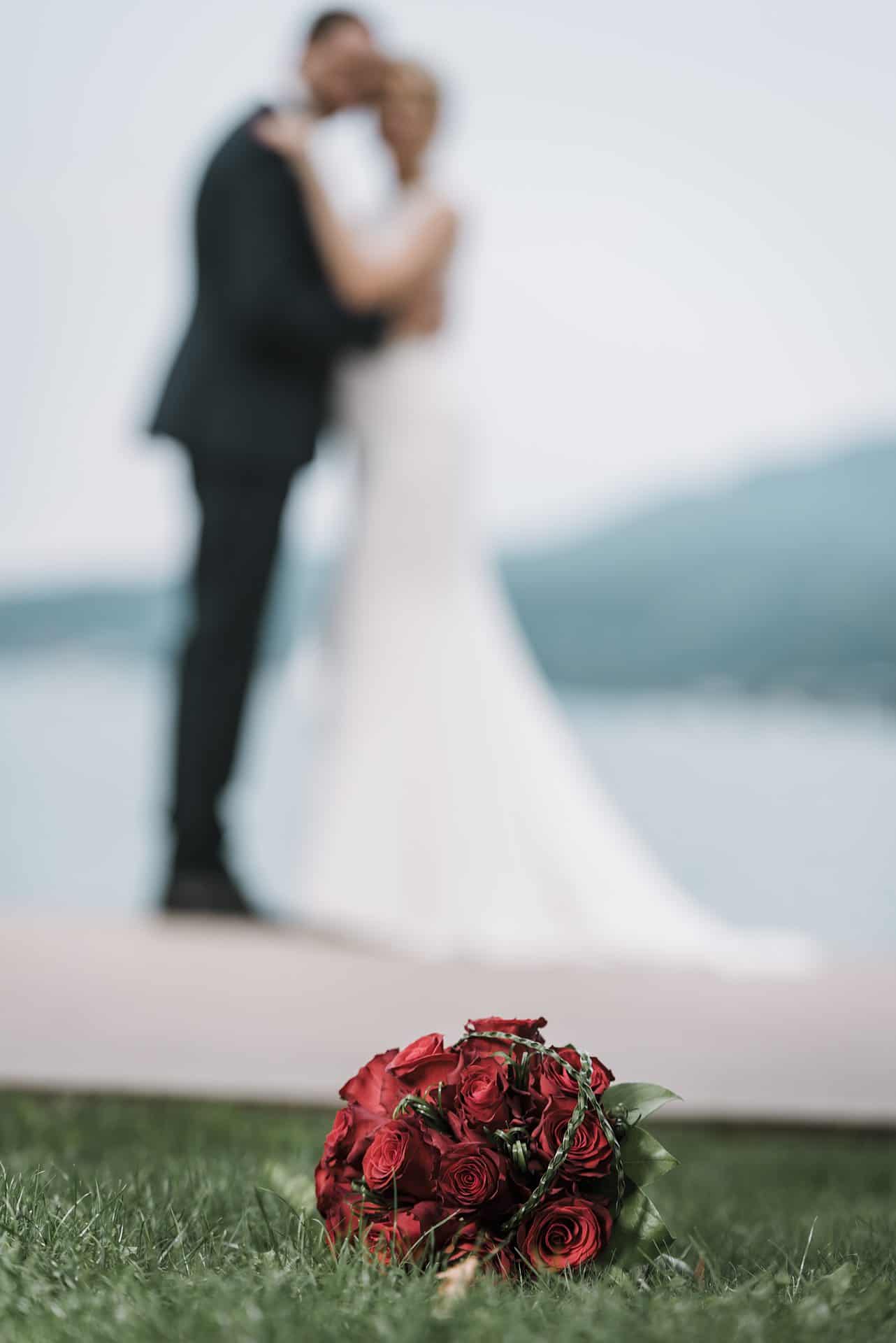 Eine Braut und ein Bräutigam stehen neben einem Strauß roter Rosen.