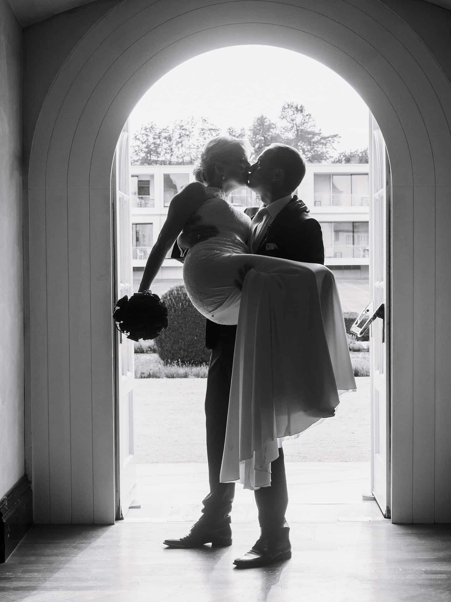 Eine Braut und ein Bräutigam küssen sich in einem Torbogen.