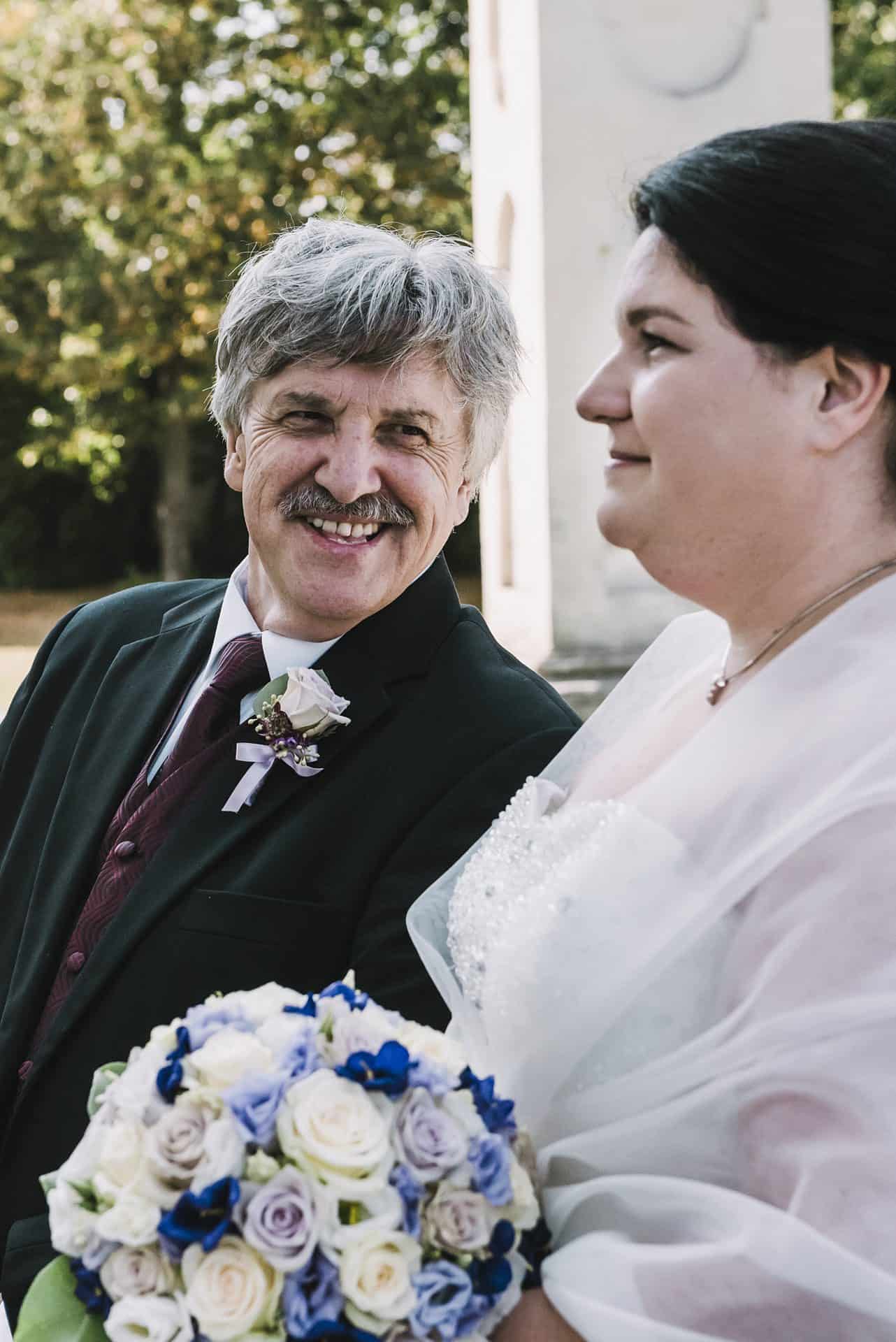 Eine Braut und ein Bräutigam lächeln vor einem Denkmal.