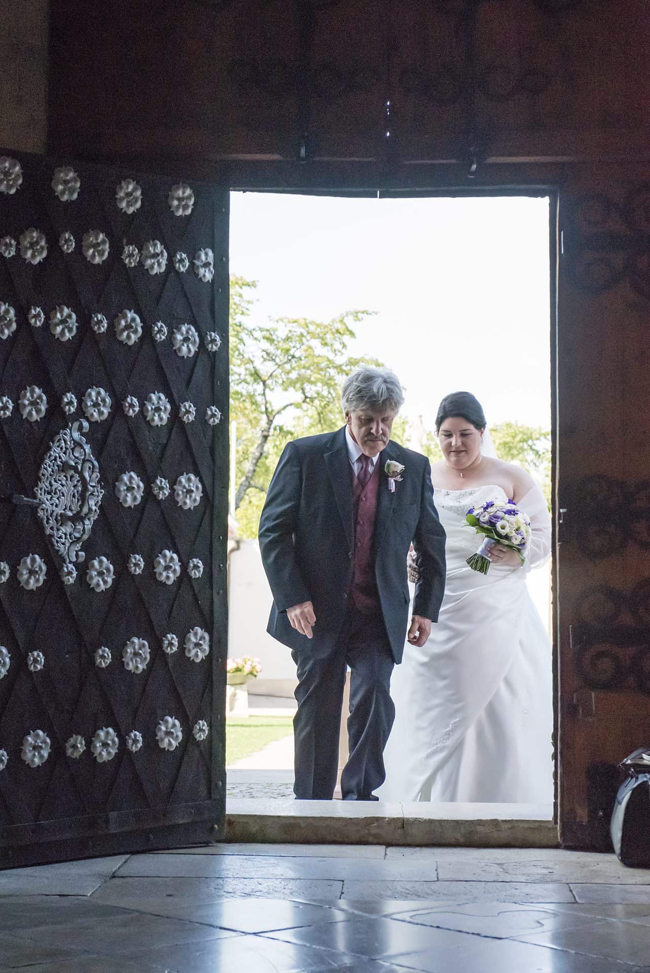 Eine Braut und ihr Vater gehen aus einer reich verzierten Tür.