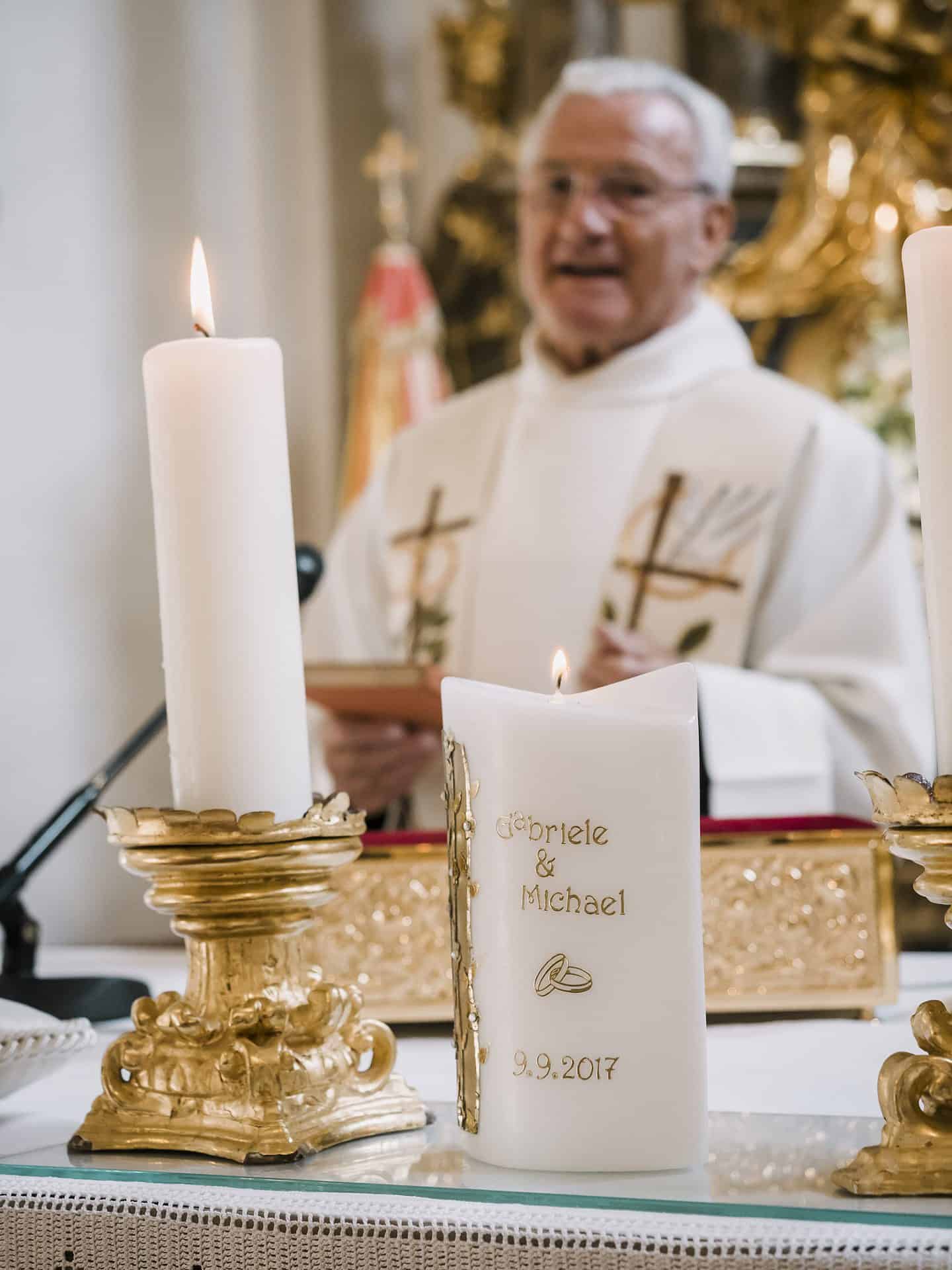 Ein Priester hält Kerzen vor einem goldenen Altar.