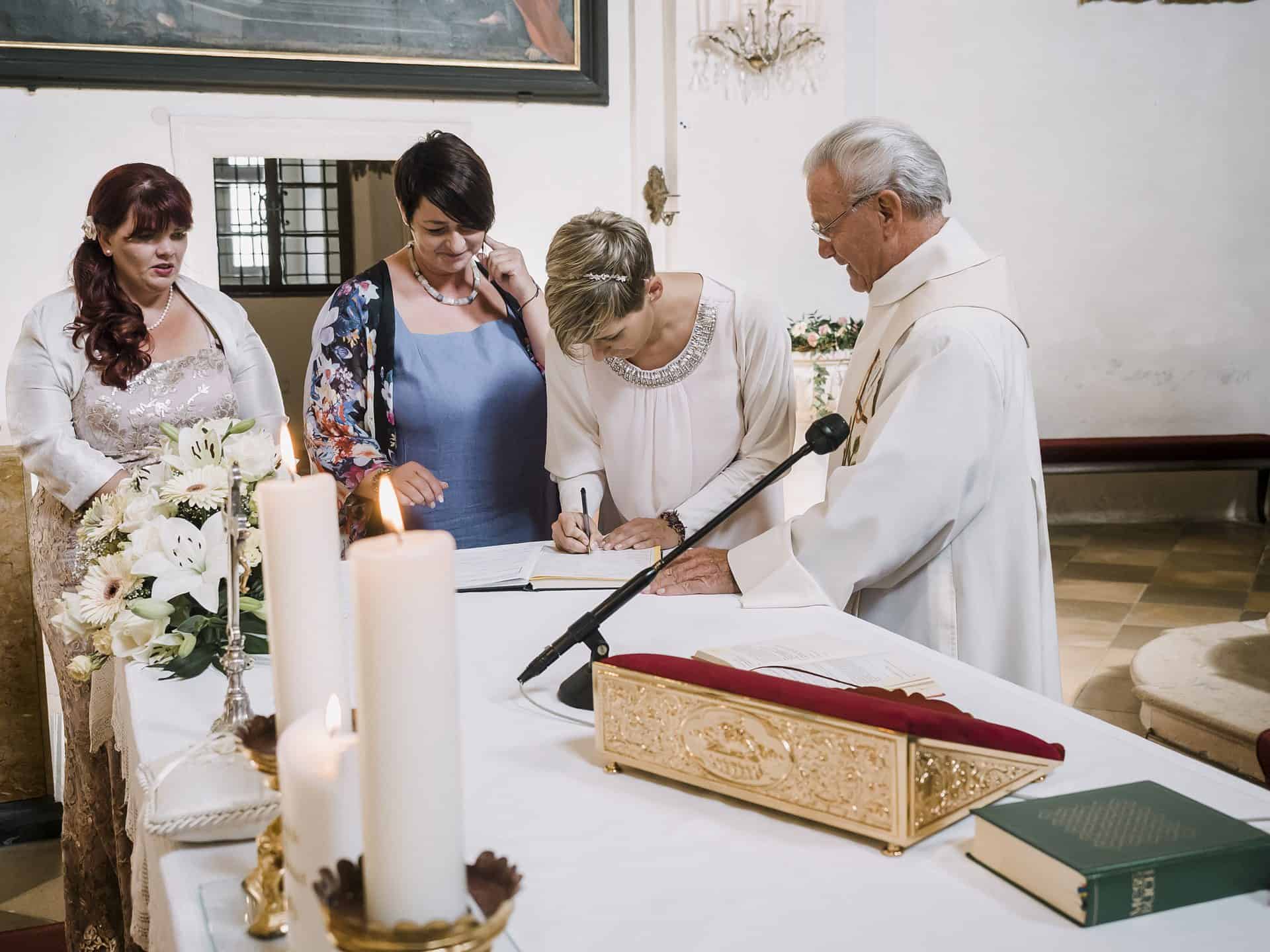 Ein Priester unterschreibt vor einer Gruppe von Menschen eine Heiratsurkunde.