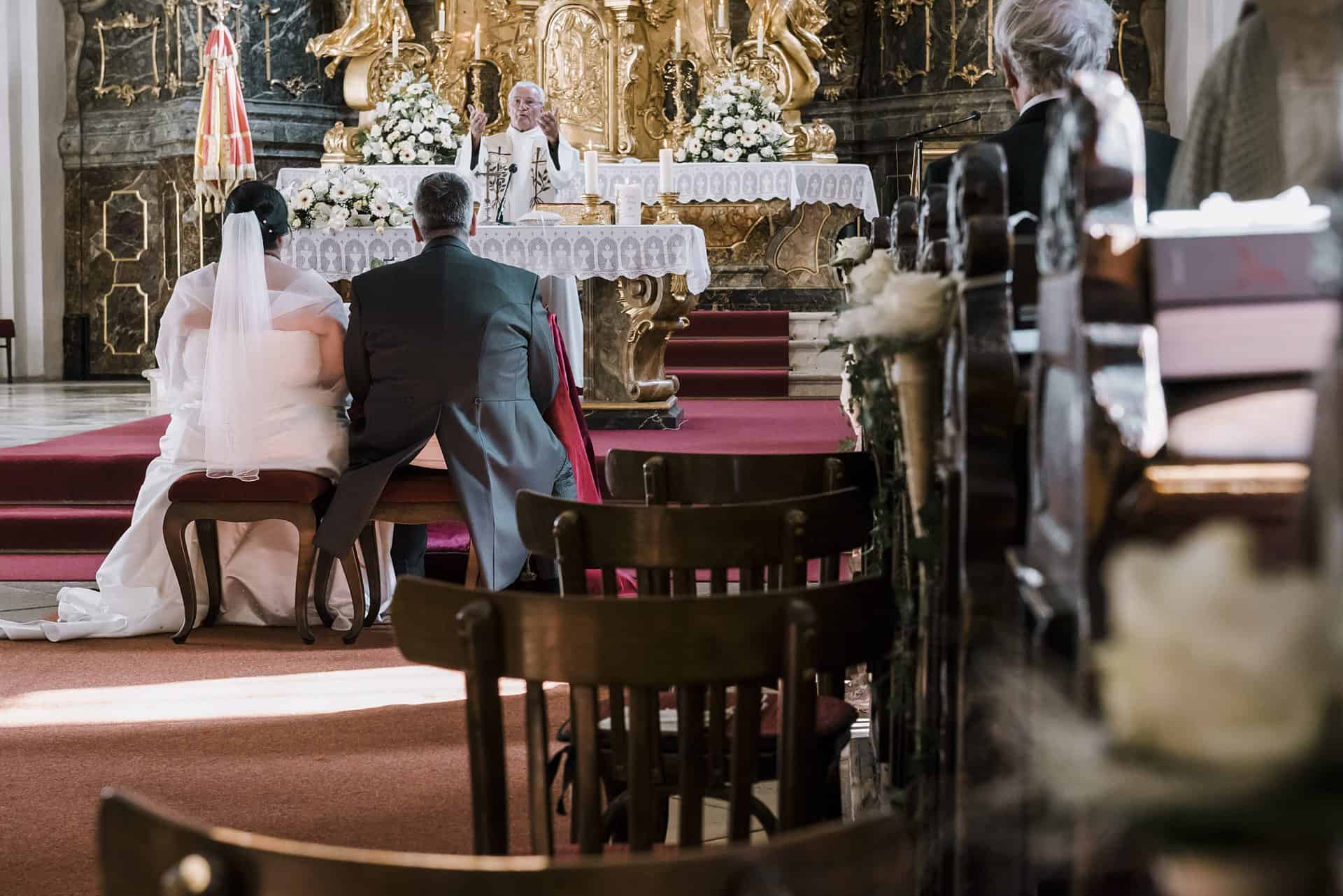 Eine Hochzeitszeremonie in einer Kirche mit Braut und Bräutigam, die in den Kirchenbänken sitzen.