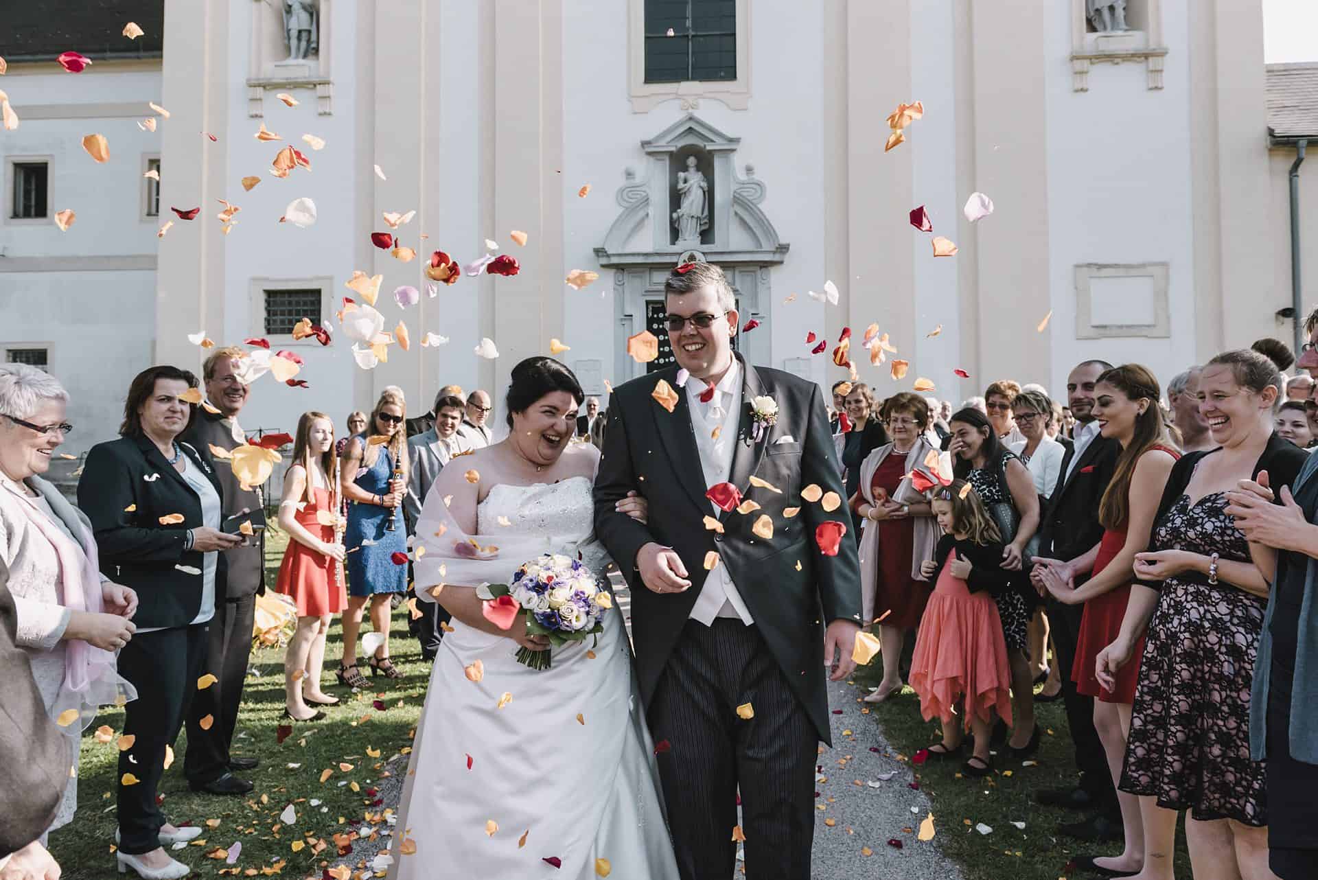 Ein Brautpaar läuft vor einer Kirche durch Konfetti.