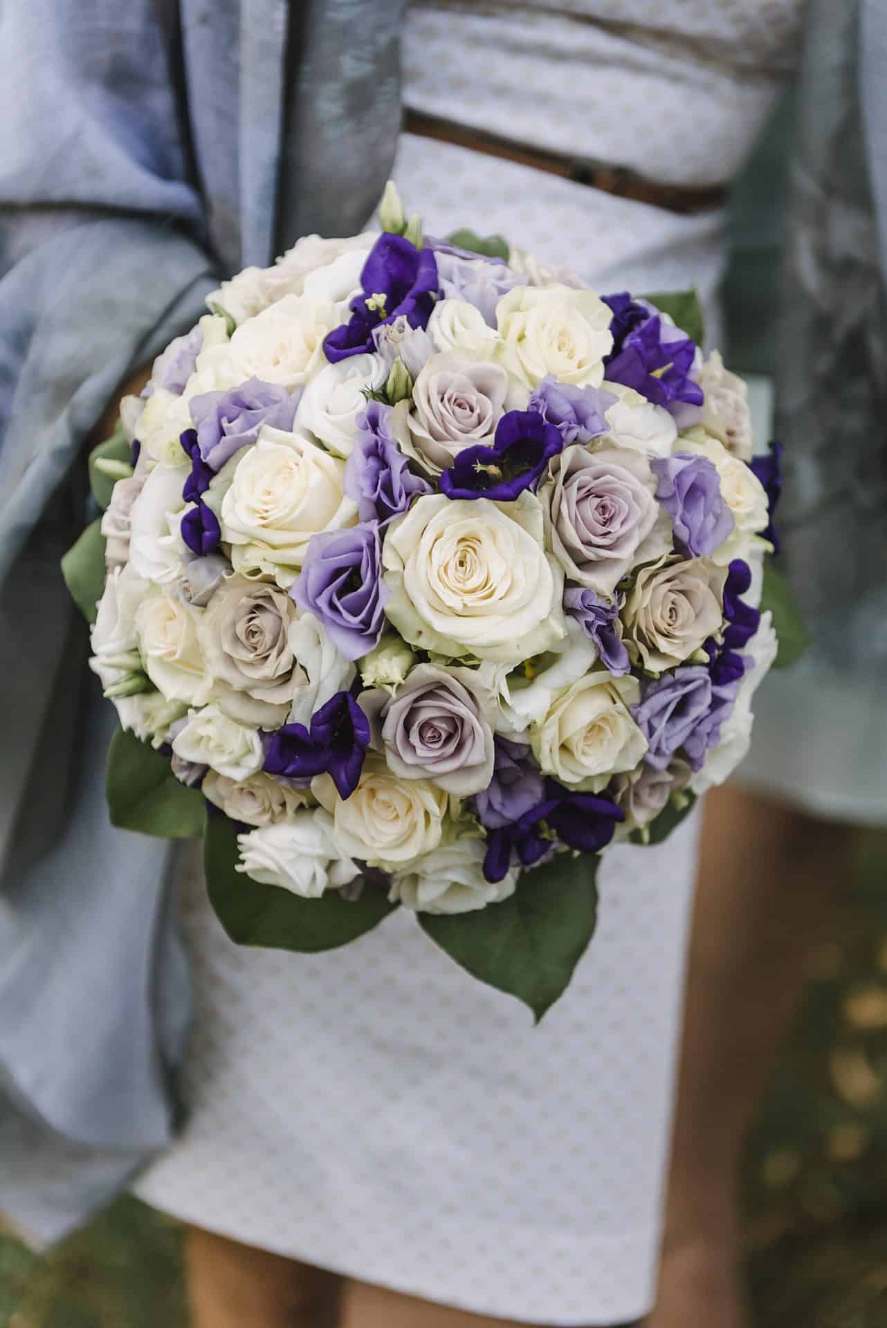 Eine Braut hält einen Strauß lila und weißer Rosen.