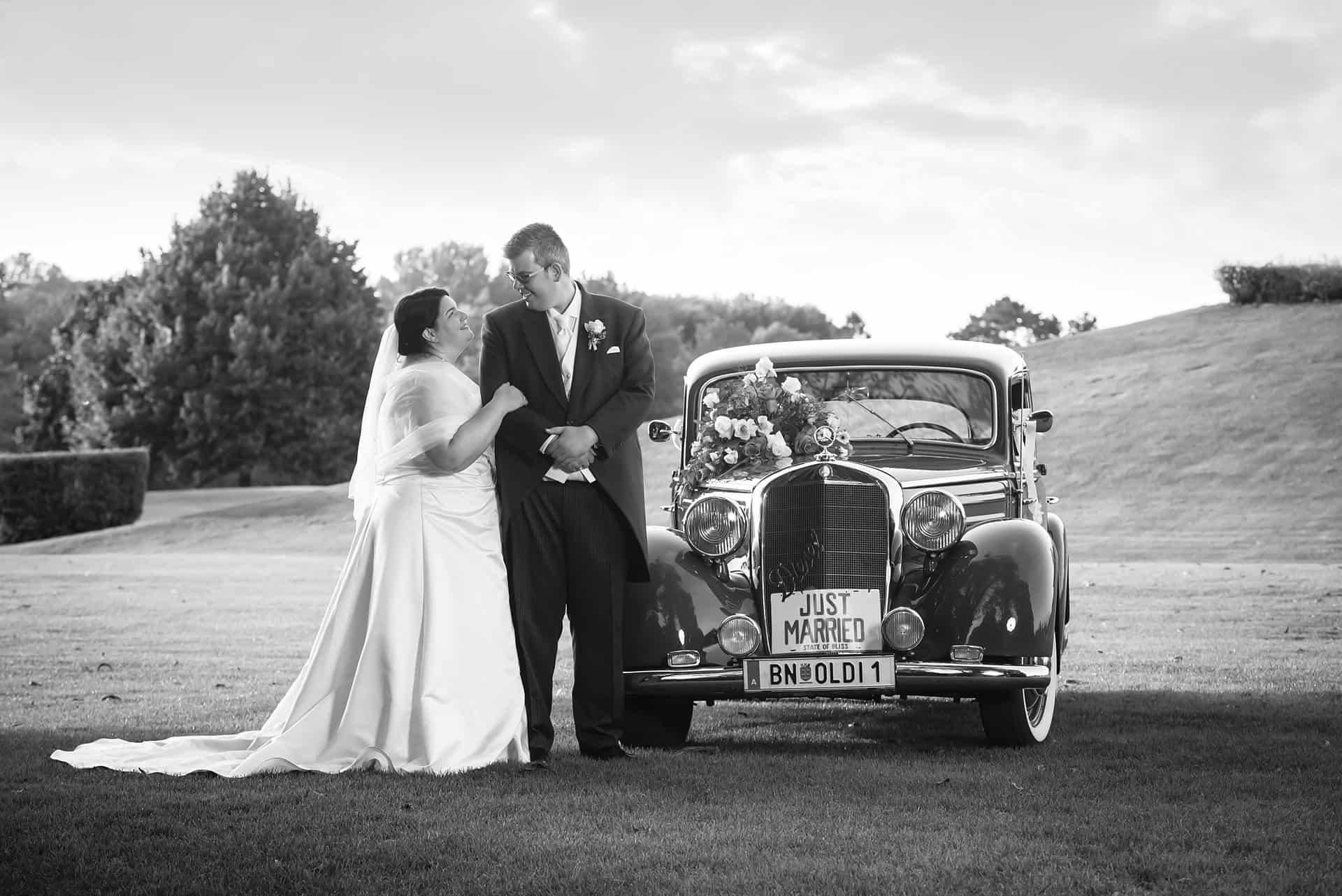 Eine Braut und ein Bräutigam stehen neben einem alten Auto.