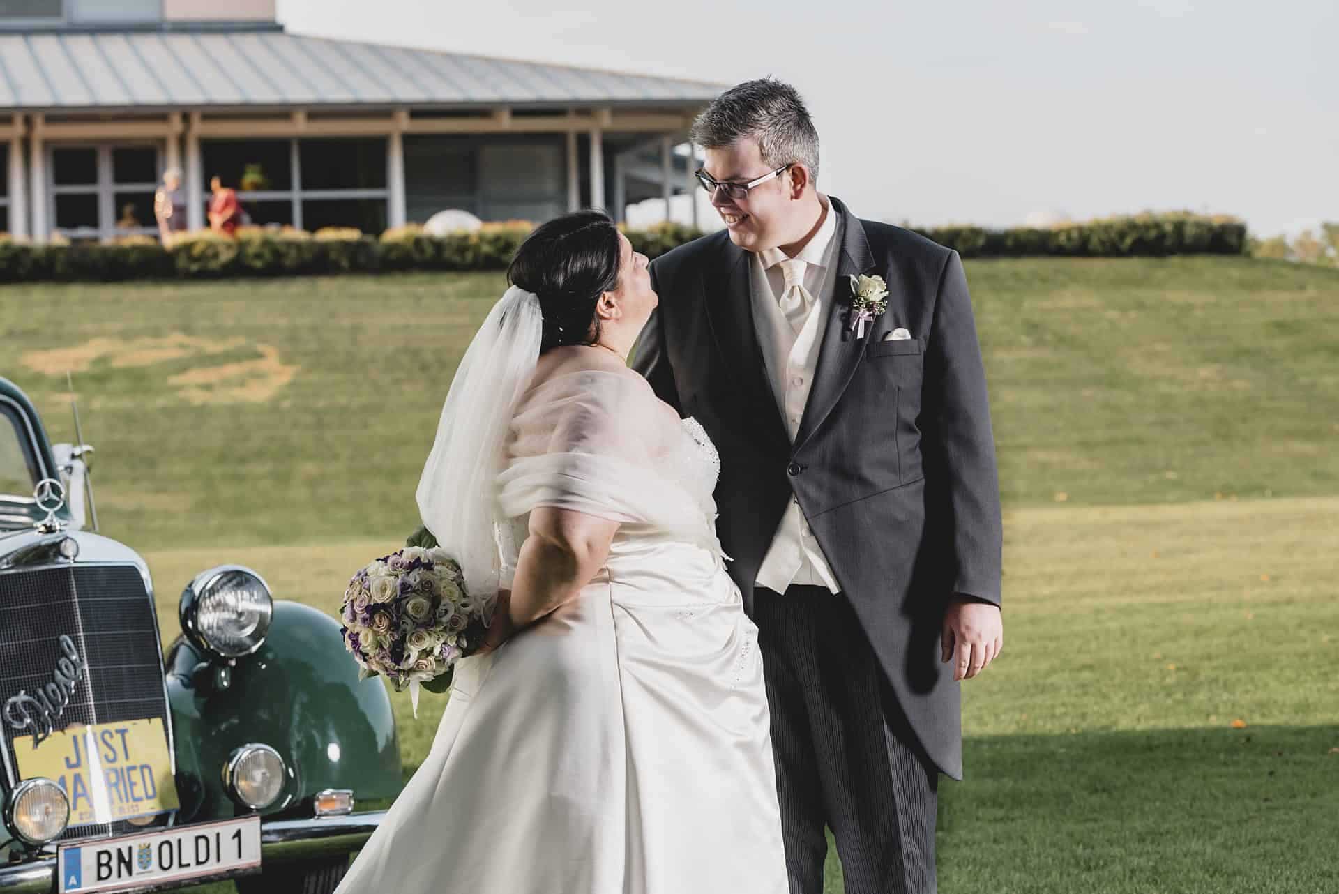 Eine Braut und ein Bräutigam stehen neben einem Oldtimer.