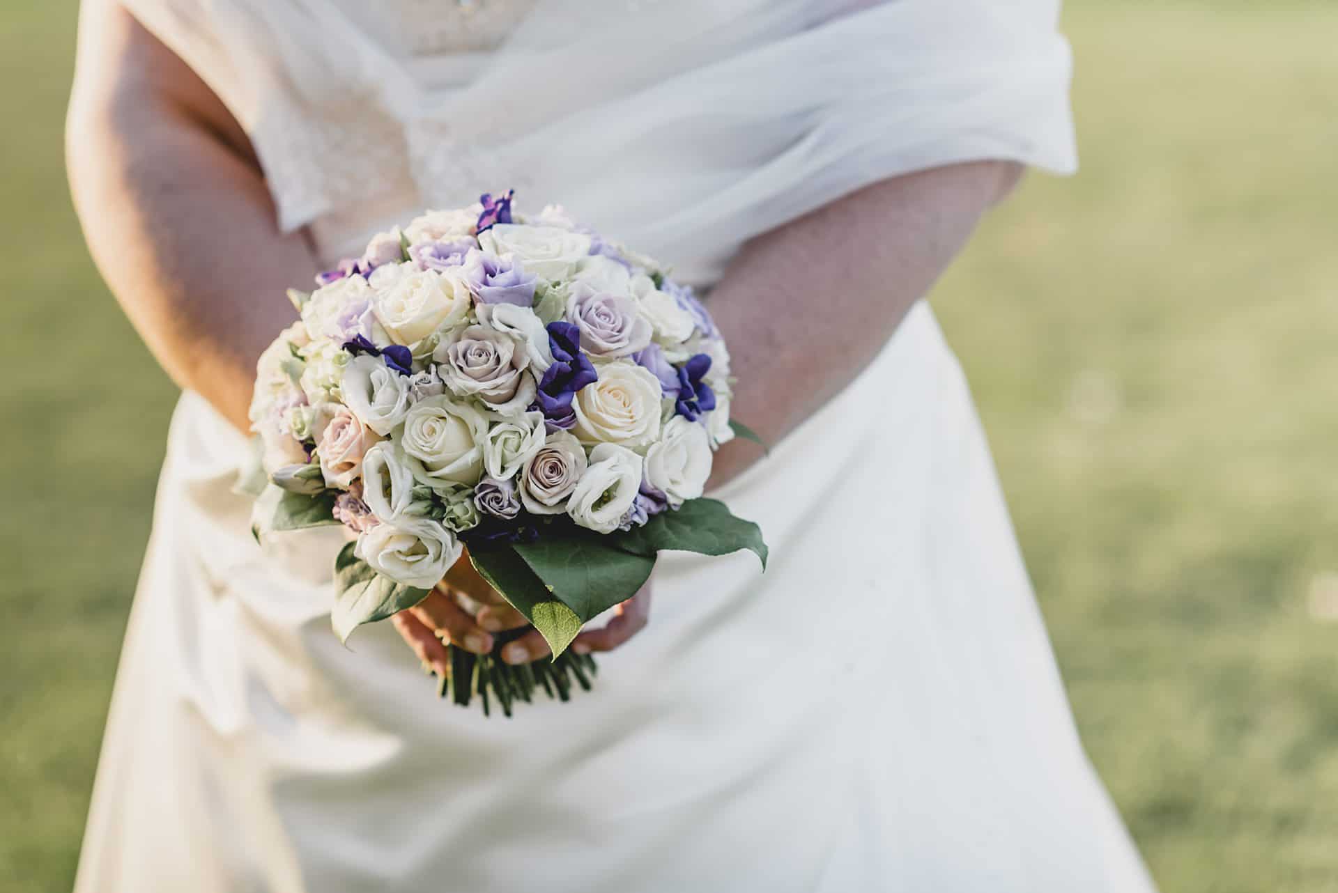 Eine Braut hält einen Strauß lila und weißer Blumen.