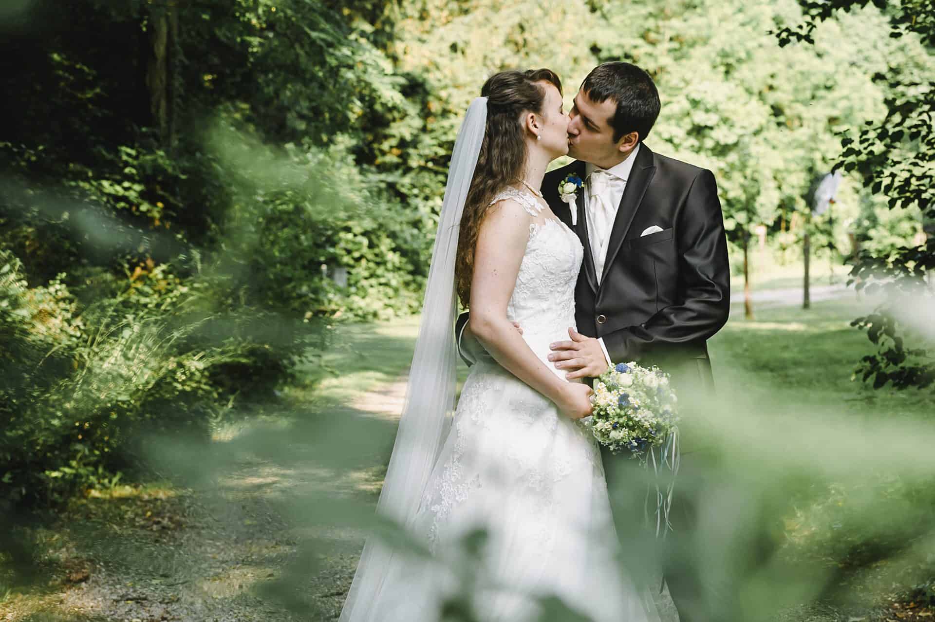 Eine Braut und ein Bräutigam küssen sich im Wald.
