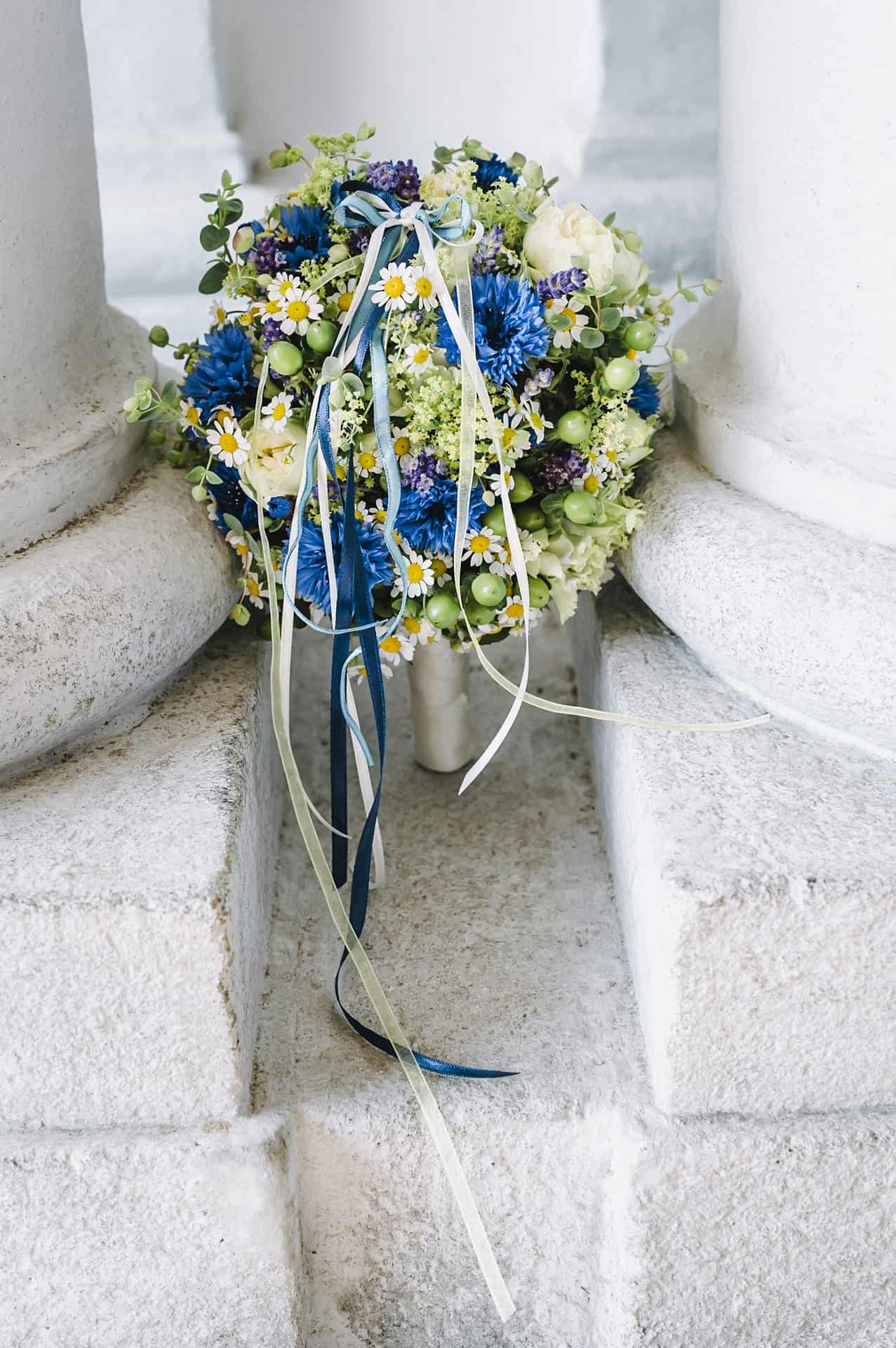Auf einer Säule sitzt ein Strauß blau-weißer Blumen.