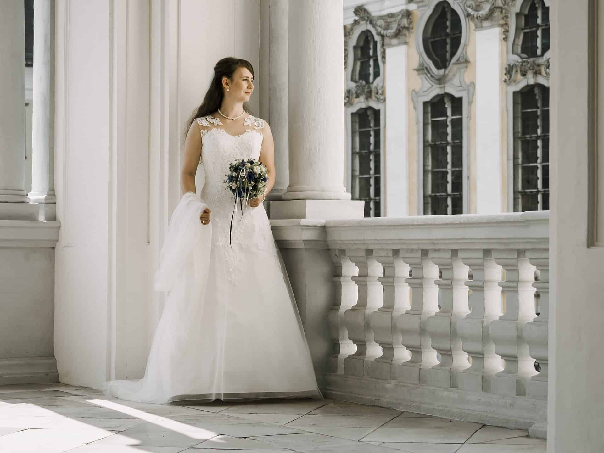 Eine Braut in einem weißen Hochzeitskleid steht auf einem Balkon.