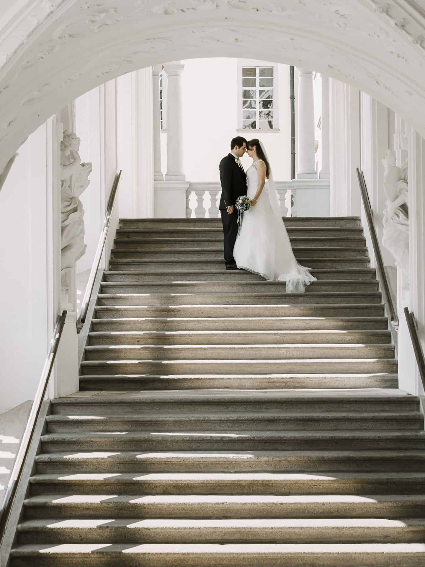 Eine Braut und ein Bräutigam stehen auf den Stufen eines reich verzierten Gebäudes.