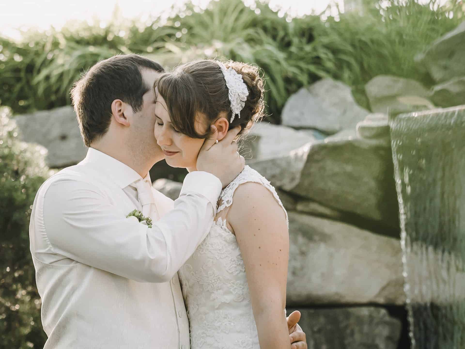 Eine Braut und ein Bräutigam küssen sich vor einem Wasserfall.