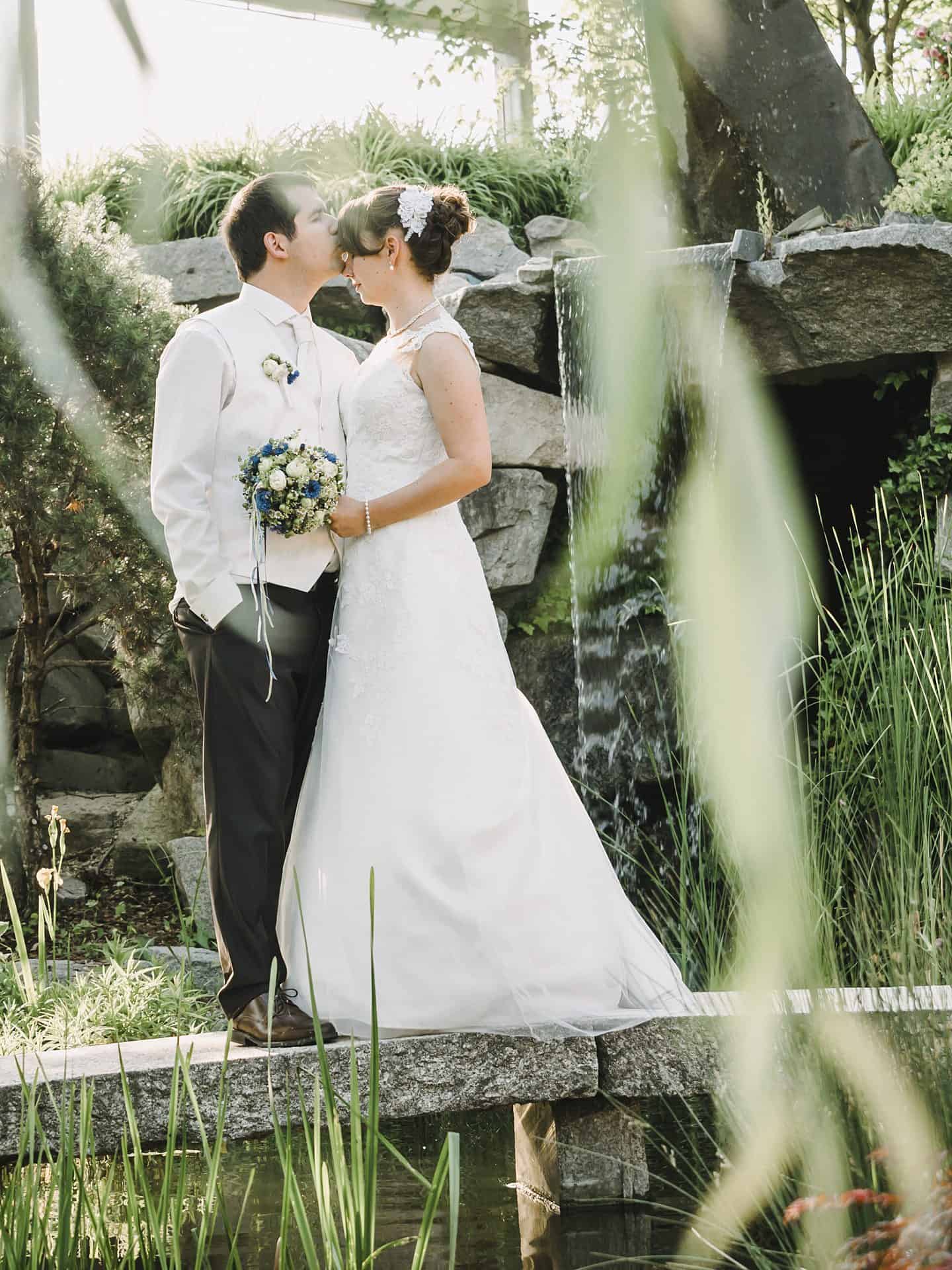 Ein Brautpaar küsst sich vor einem Teich.
