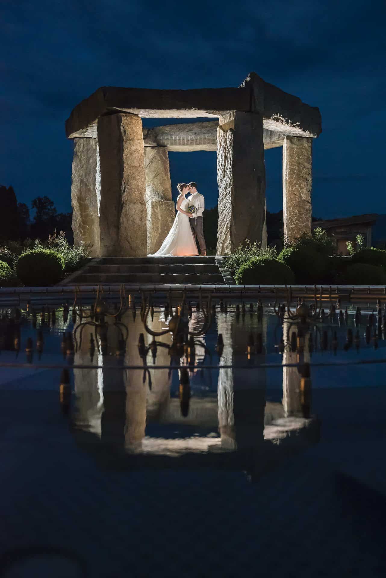 Eine Braut und ein Bräutigam stehen nachts vor einem Steingebäude.
