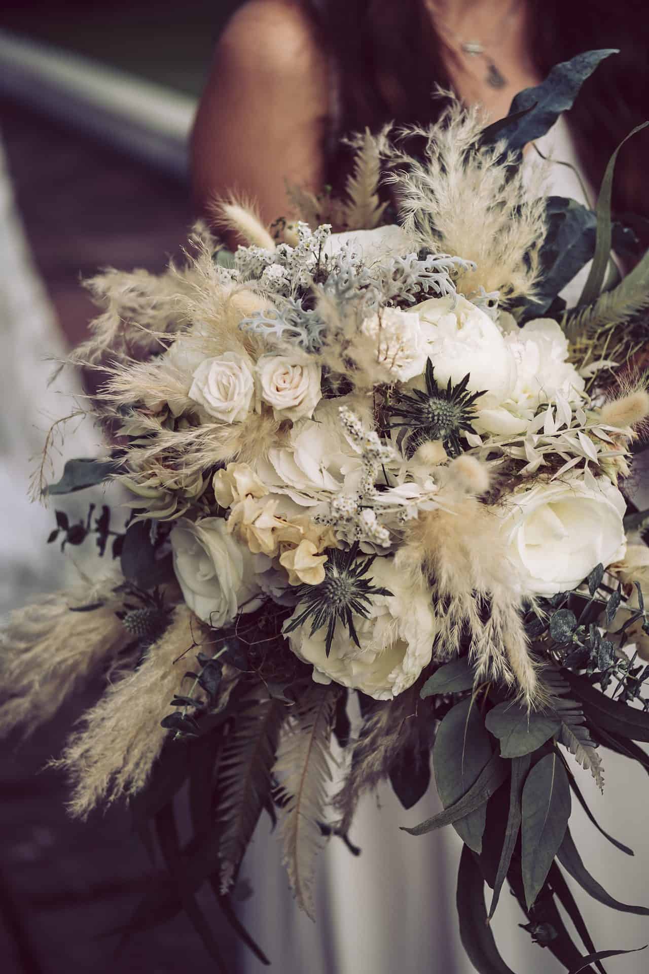 Eine Braut hält einen Strauß aus weißen Blumen und Gräsern.