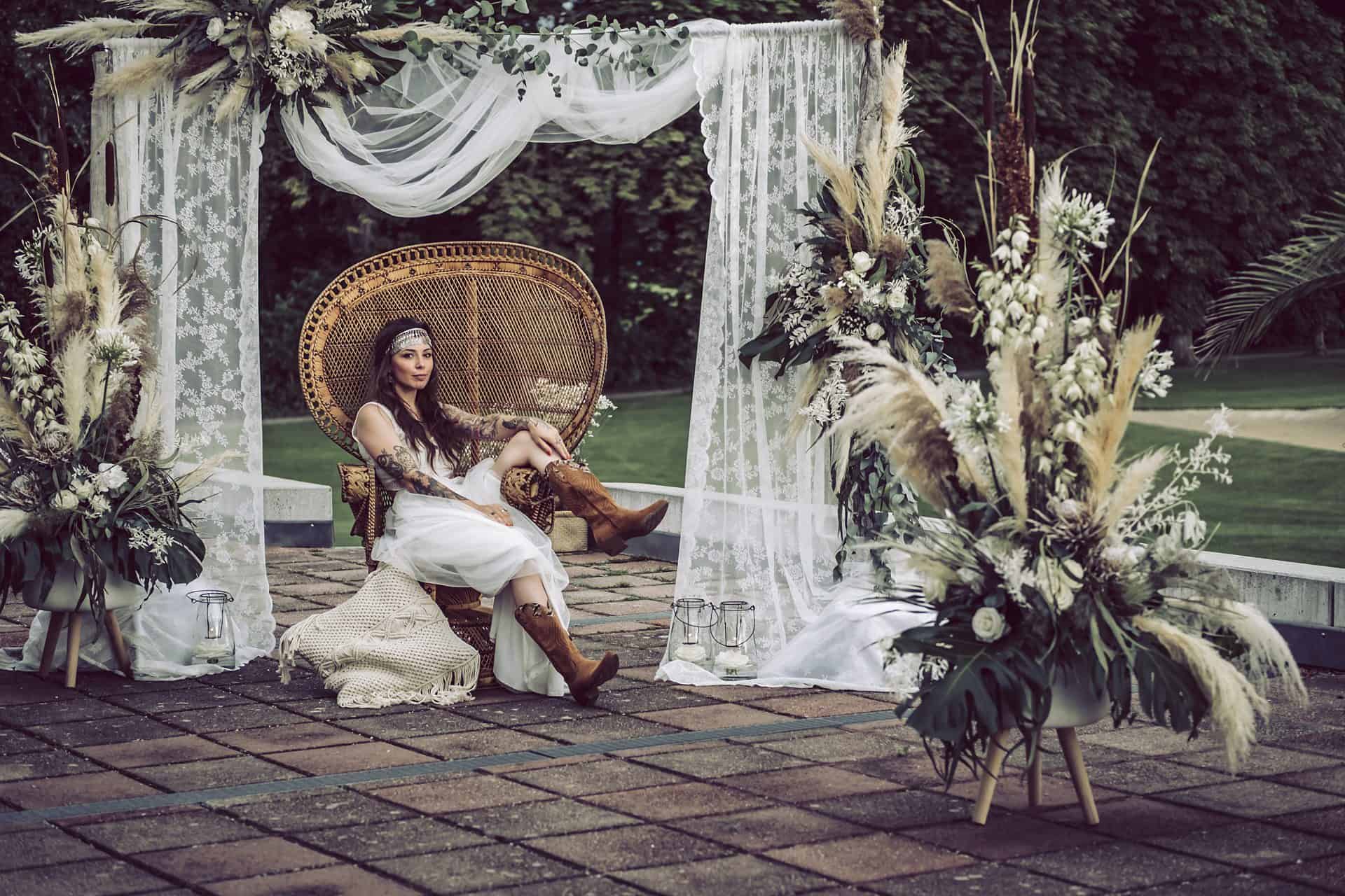 Eine Braut sitzt auf einem Stuhl vor einem Blumenarrangement.