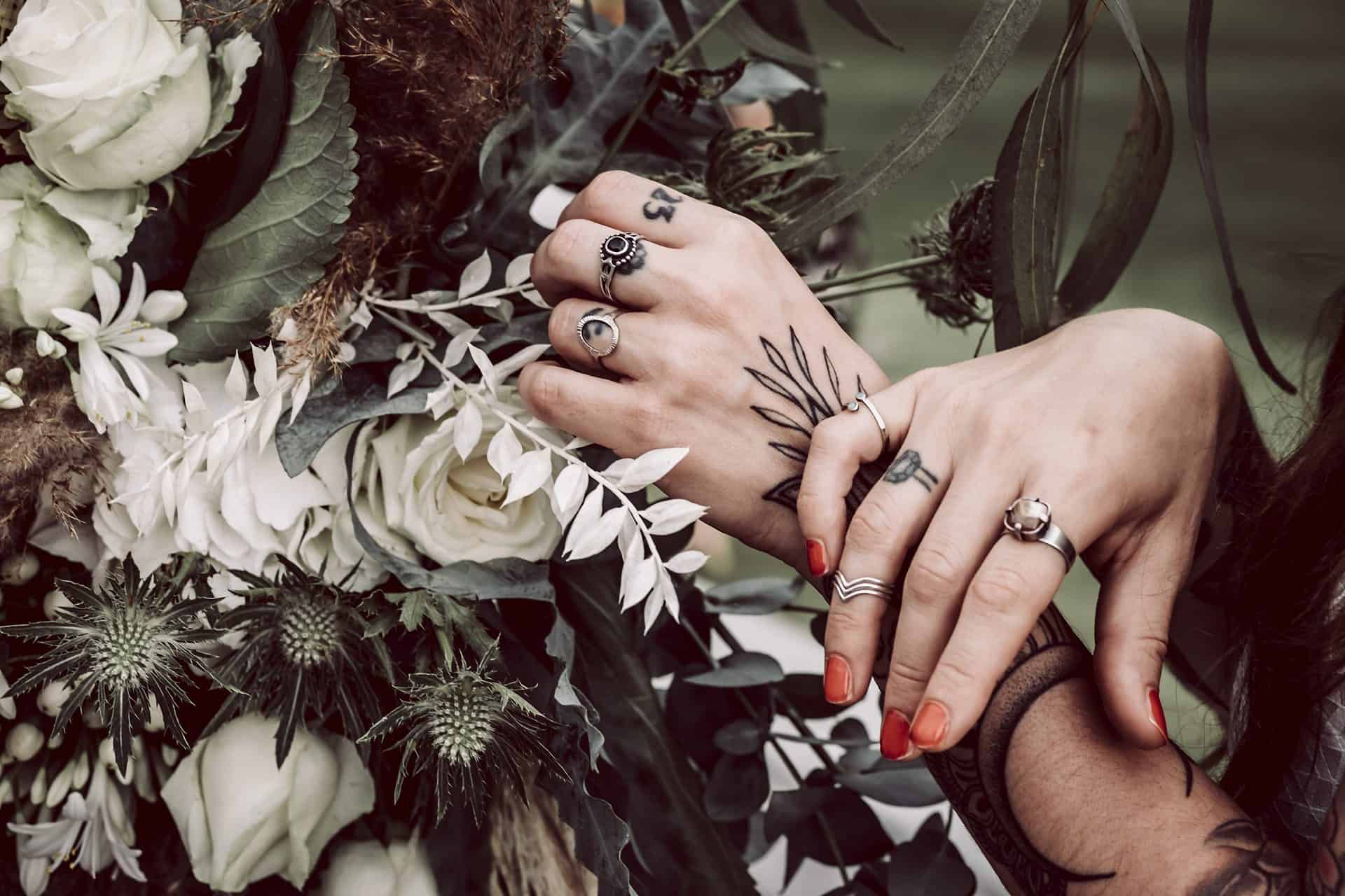 Eine Frau mit Tätowierungen und Ringen hält einen Blumenstrauß in der Hand.