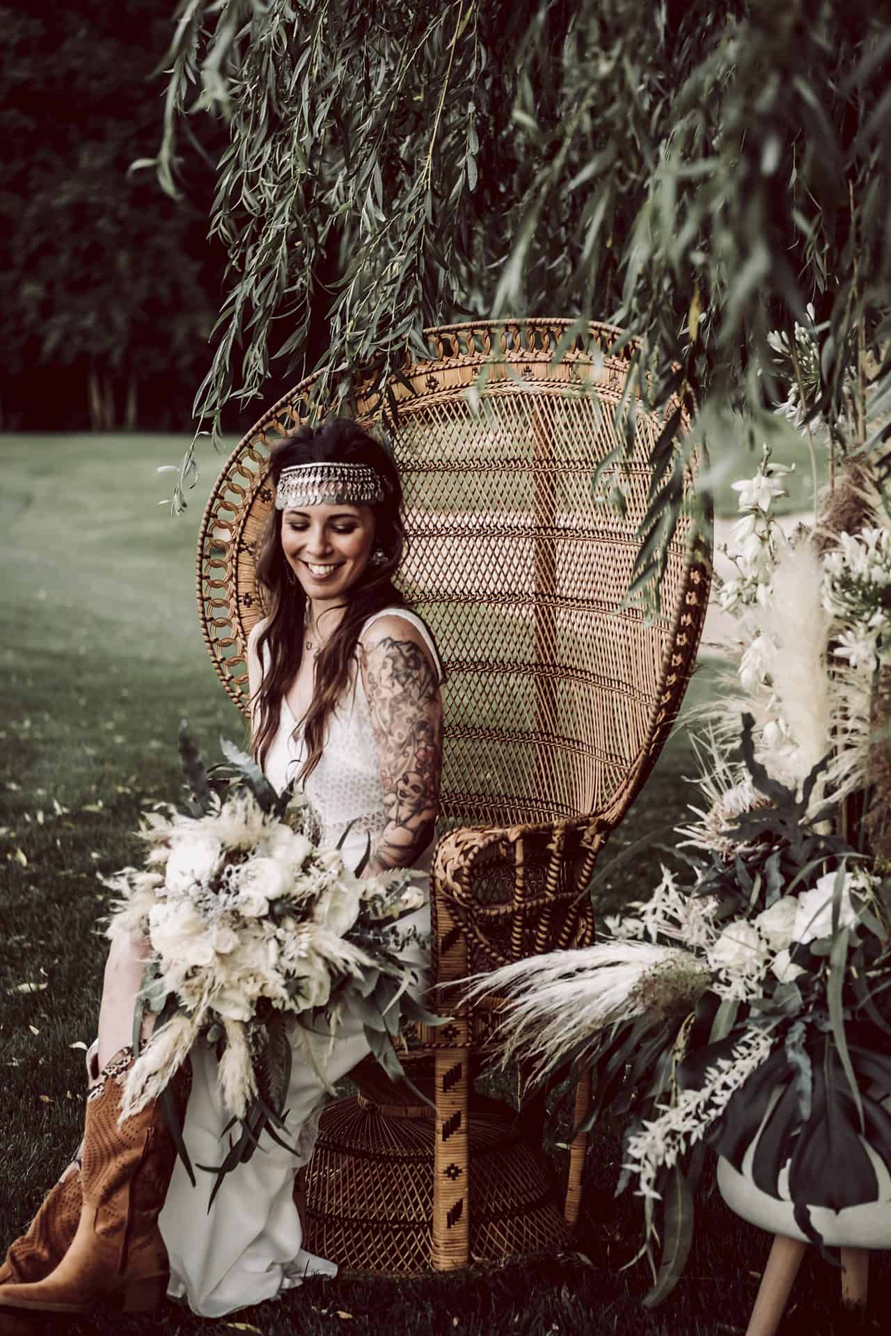 Eine Braut sitzt in einem Korbstuhl mit einem Blumenstrauß.