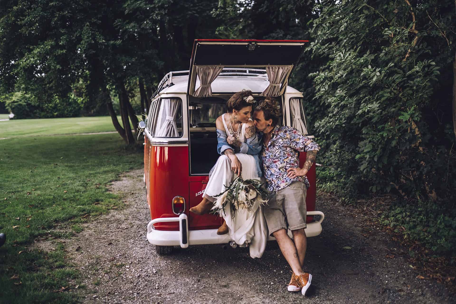 Eine Braut und ein Bräutigam posieren vor einem VW-Wohnmobil.