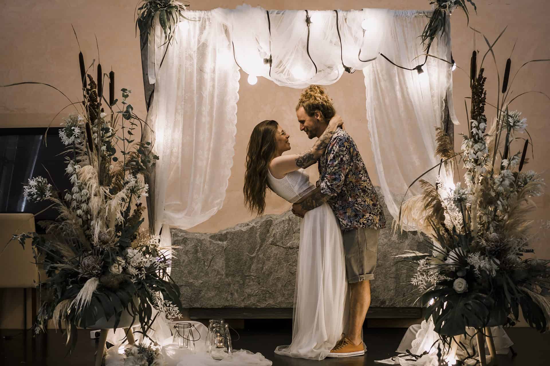 Eine Braut und ein Bräutigam küssen sich unter einem Hochzeitsbogen.