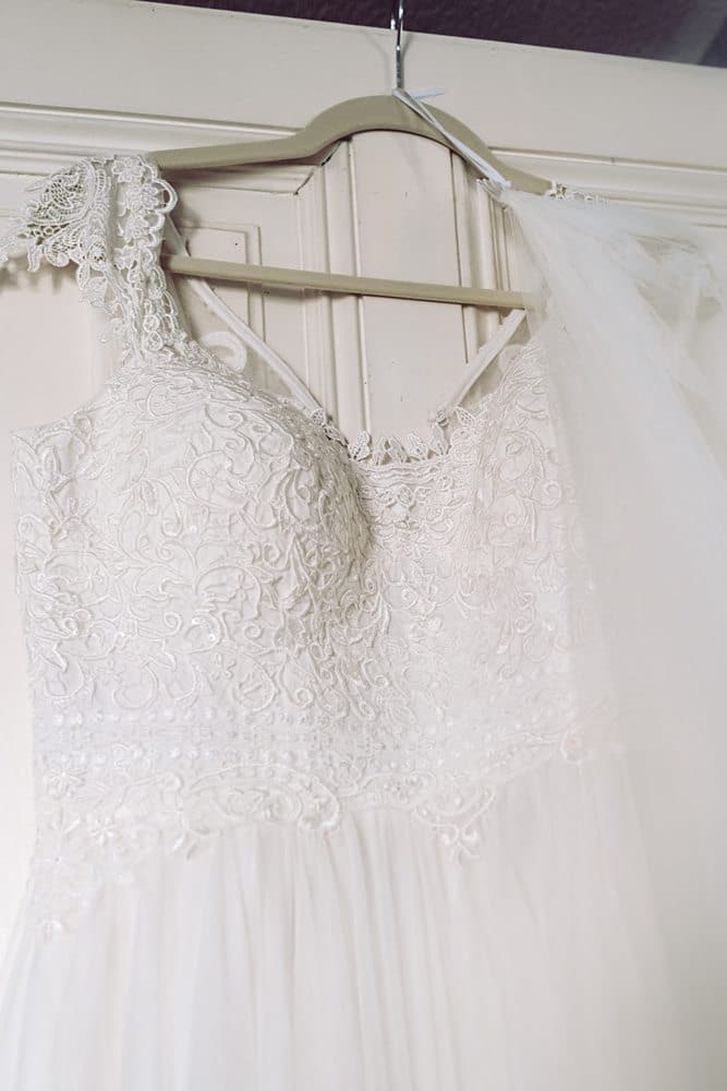 Ein weißes Hochzeitskleid hängt an einem Kleiderbügel.