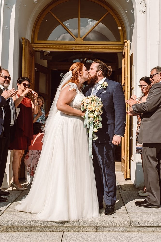 Eine Braut und ein Bräutigam küssen sich außerhalb einer Kirche.