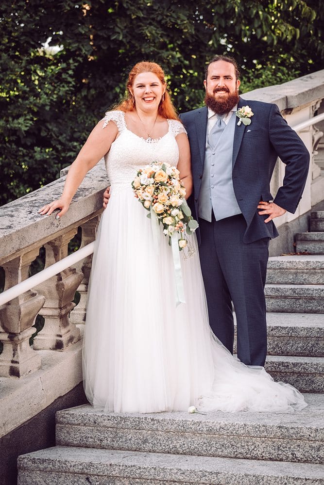 Eine Braut und ein Bräutigam posieren auf den Stufen eines Parks.